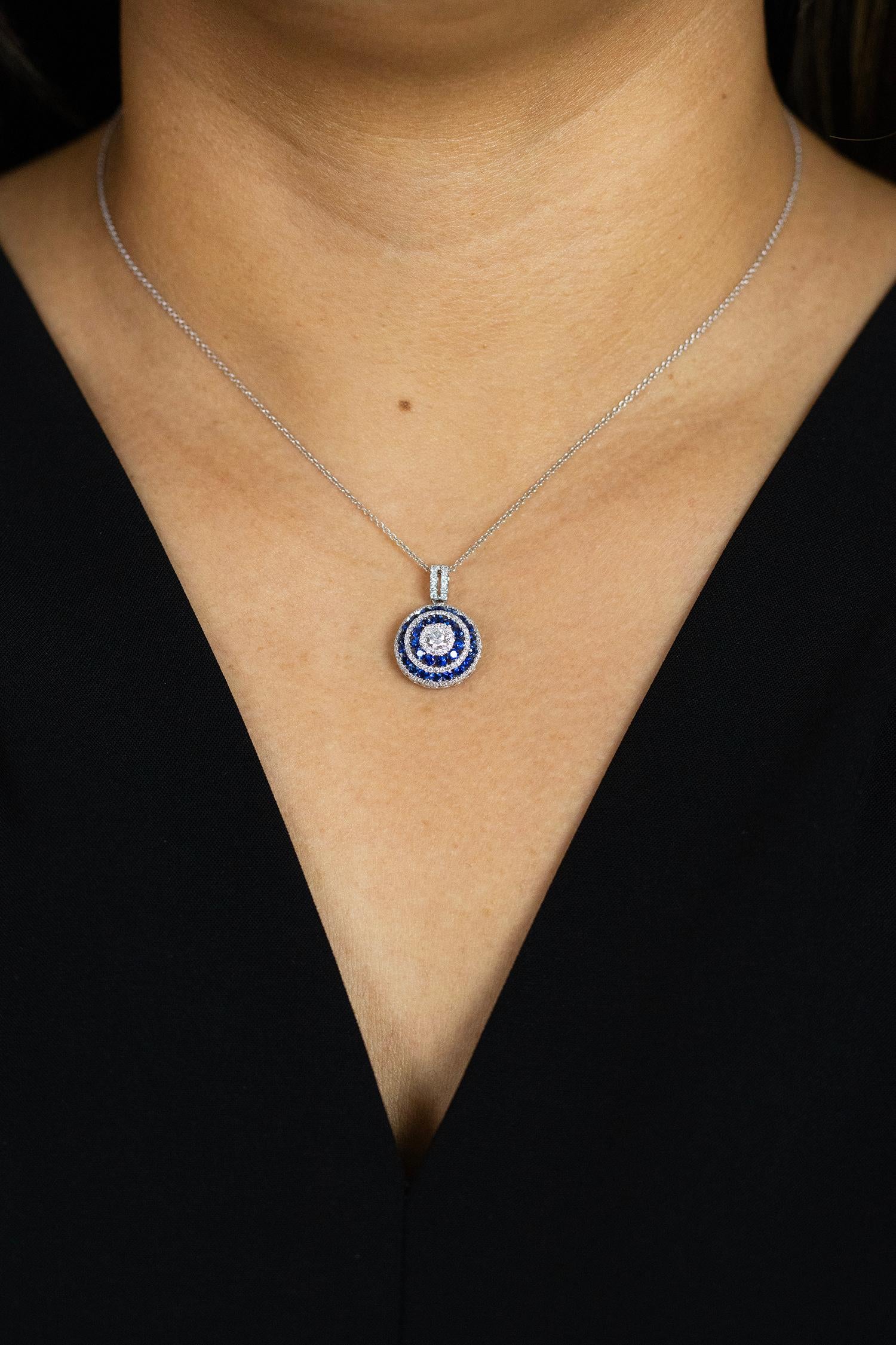A unique and stylish pendant necklace showcasing a round brilliant diamond center, accented by rows of round diamonds and blue sapphires. Diamonds weigh 0.63 carats total; blue sapphires weigh 1.17 carats total. Made in 18k white gold.

Roman