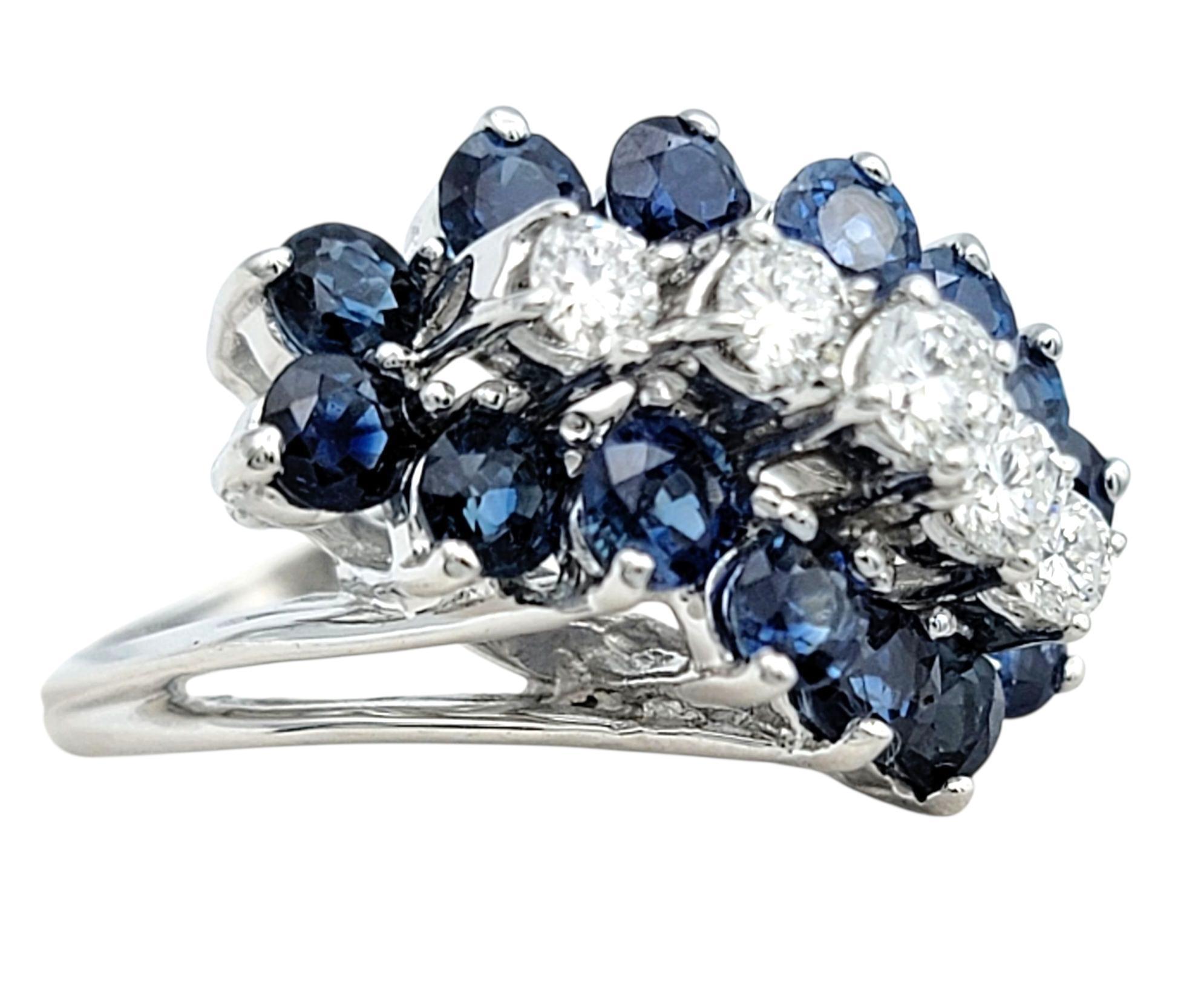 Dieser bezaubernde Ring mit Saphiren und Diamanten verkörpert klassische Raffinesse mit einem Hauch von königlichem Flair. Der aus 14 Karat Weißgold gefertigte Ring zeigt in der Mitte eine Ansammlung tiefblauer Saphire, die von schimmernden