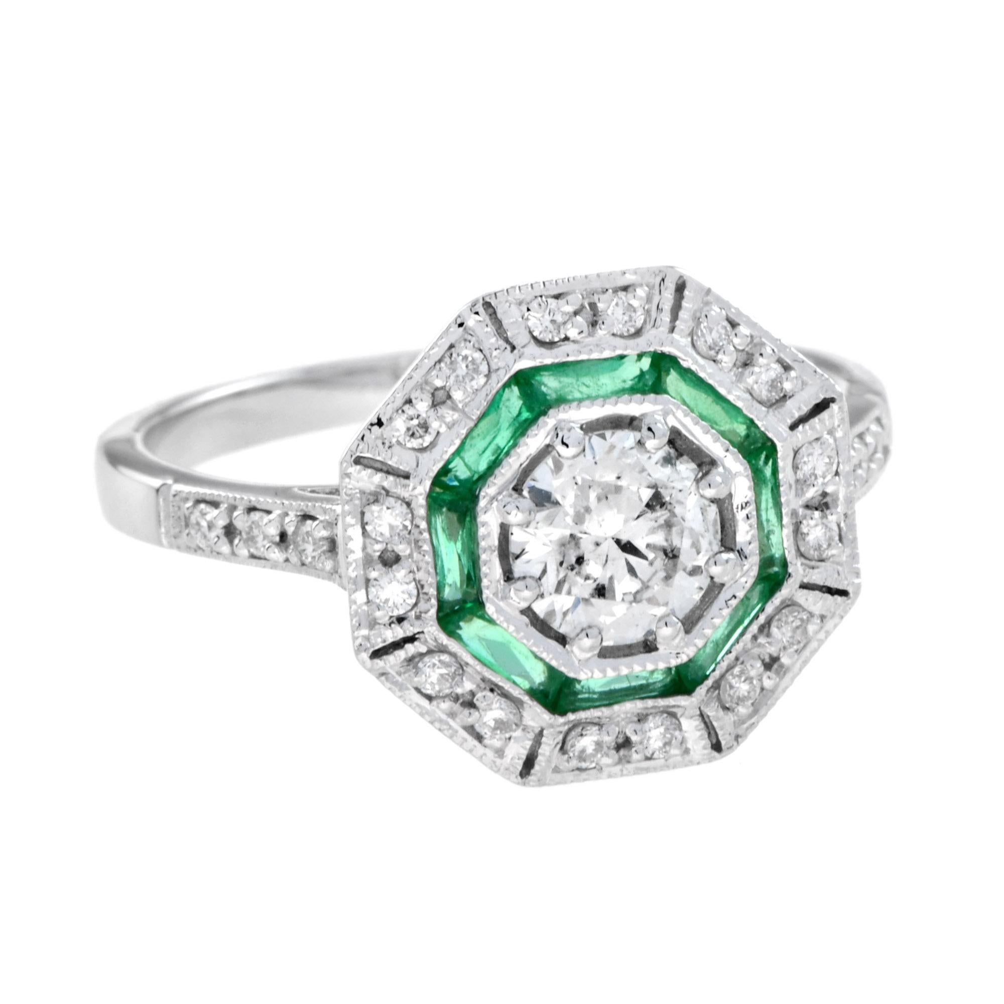 A stunning center diamond surrounded by an outer ring of round diamonds. The inner ring is adorned with French-cut emeralds, adding a vibrant pop of color. The design is beautifully finished with delicate milgrain edging, enhancing the vintage