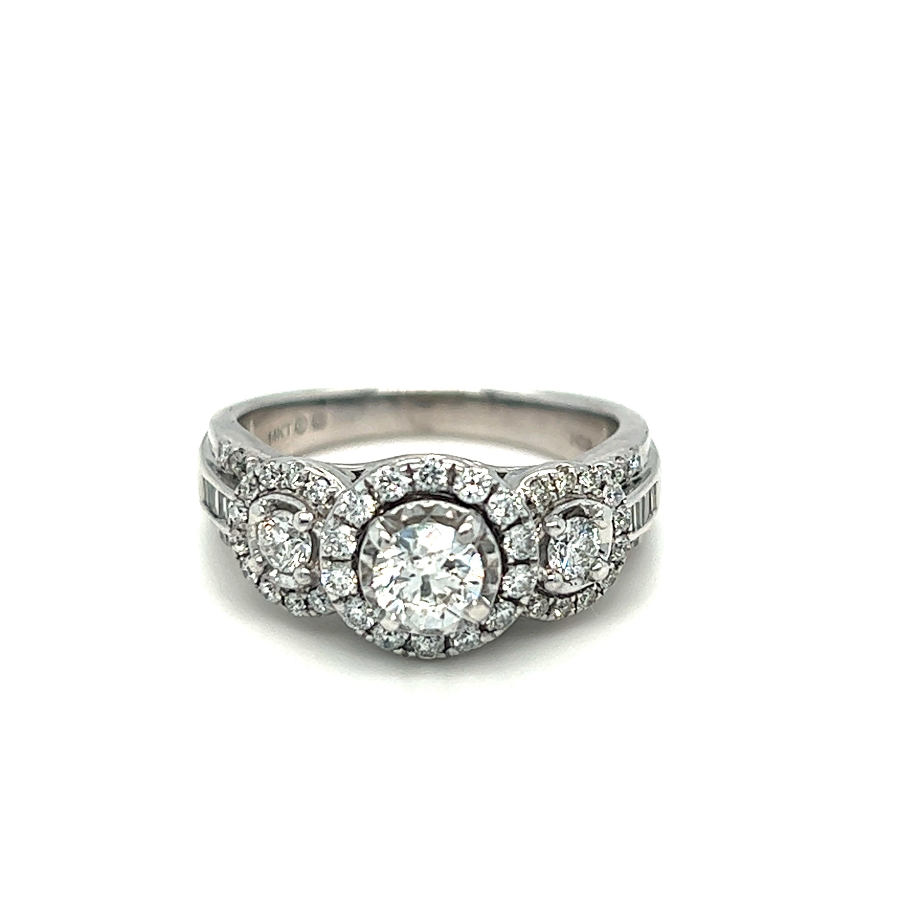 A beautiful diamond halo trilogy ring set in 14k white gold. The ring is centrally set with a round brilliant cut diamond which is claw set in an open back setting. The diamond is then flanked to each side by two perfectly matched round cut