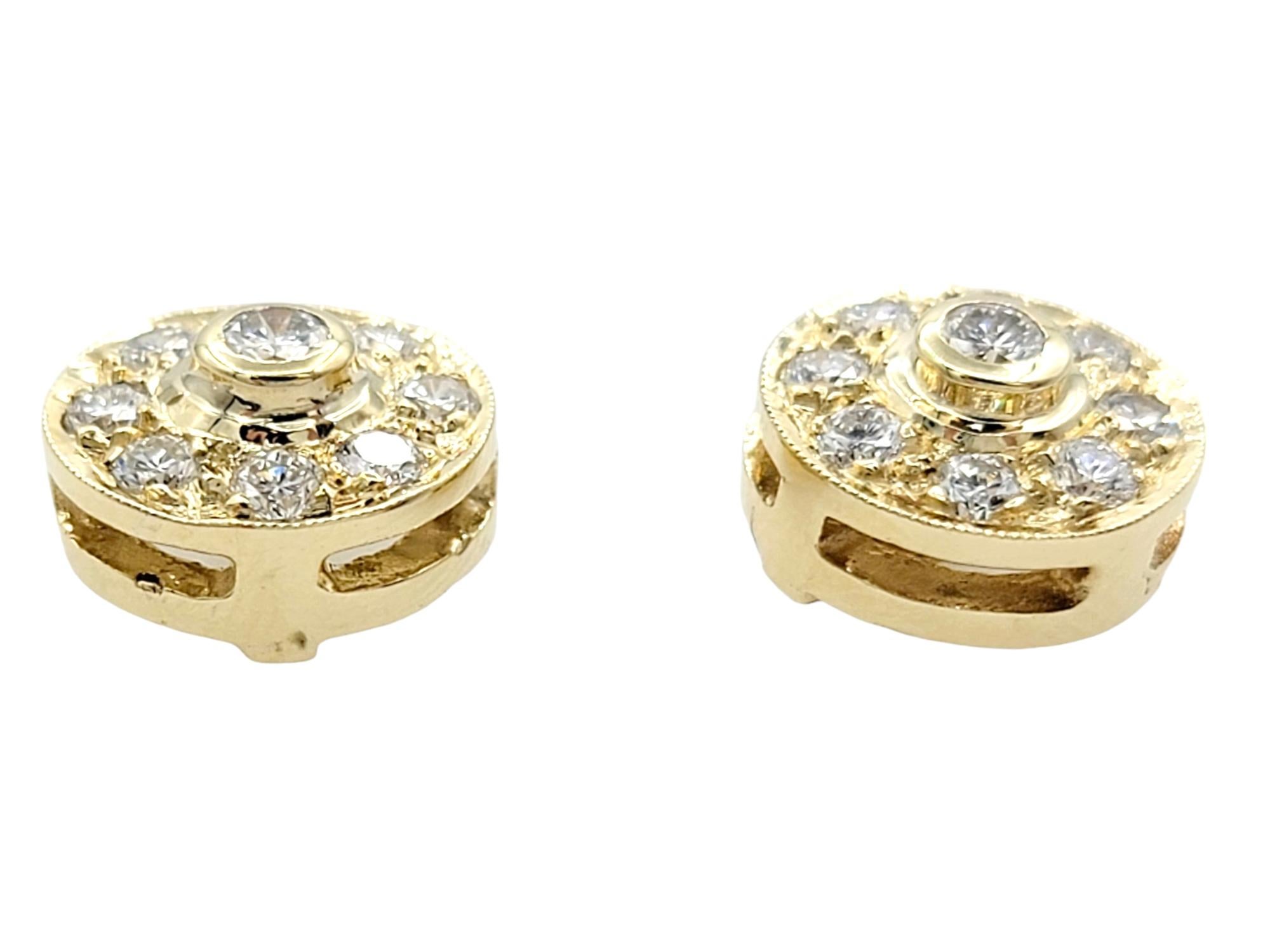 These diamond earrings, set in lustrous 14 karat yellow gold, are a radiant and captivating pair. At the center of each earring is a bezel set brilliant round diamond, serving as the focal point. Surrounding the central diamond is an array of