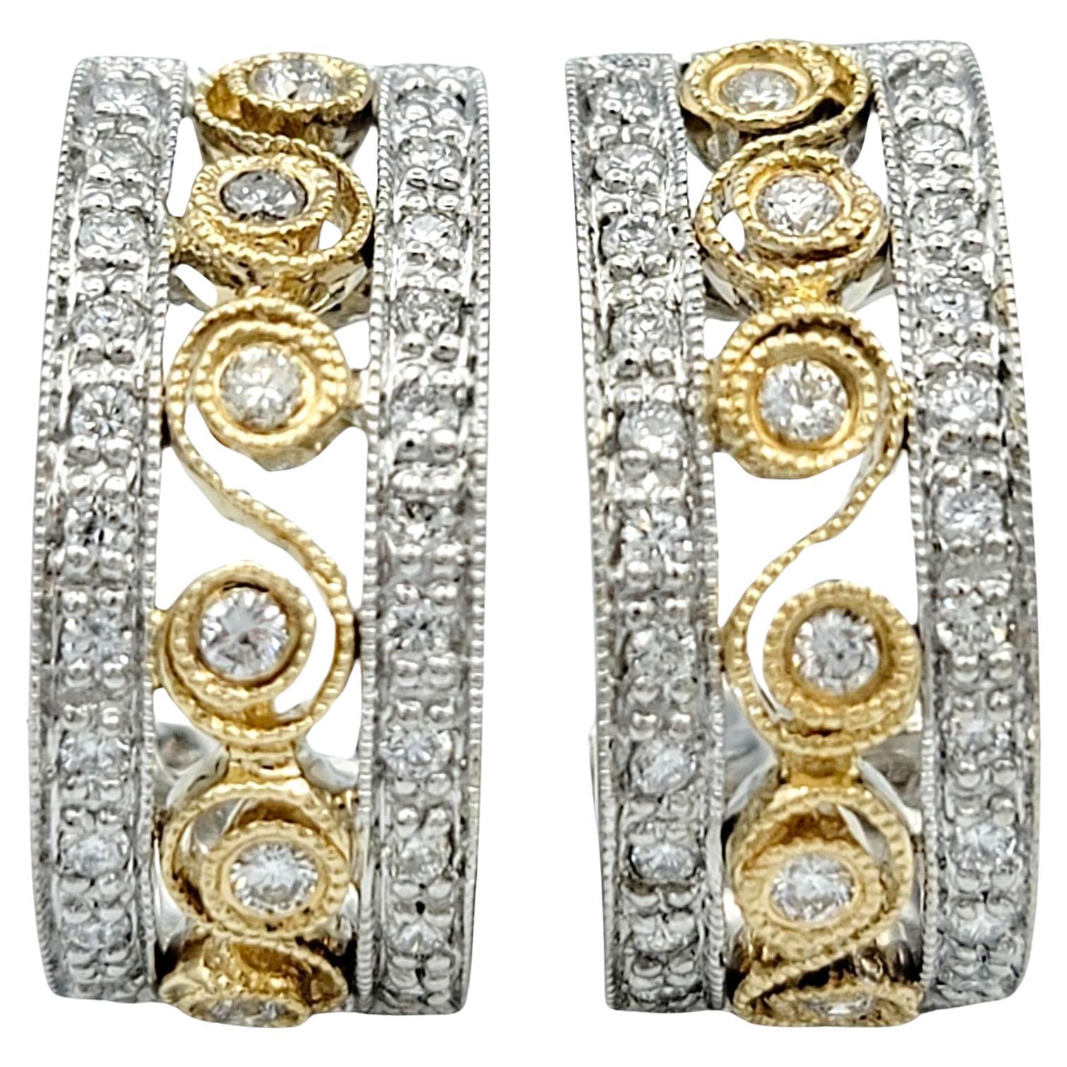This pair of J-hoop earrings, set in a beautiful combination of 14 karat yellow and white gold, showcases a sophisticated and intricate design. The center of each hoop features a column of diamonds set within a yellow gold scroll-like pattern,