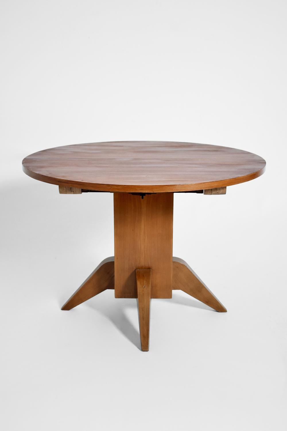 Round wooden dining table with two extensions supported by a square pillar and triangular legs. 