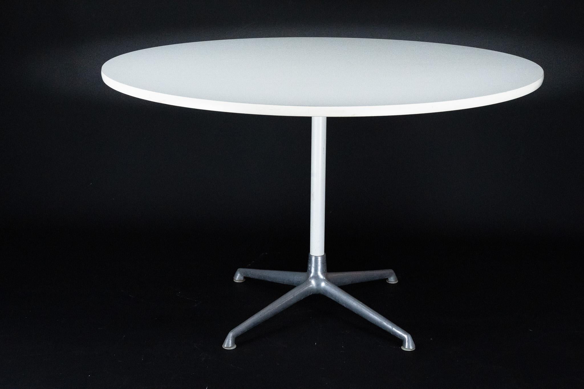 Cette élégante table de salle à manger moderne du milieu du siècle dernier présente un plateau circulaire en bois stratifié blanc soutenu par un socle en fonte d'aluminium à quatre pieds évasés. Conçu par Charles et Ray Eames. Traces normales d'âge