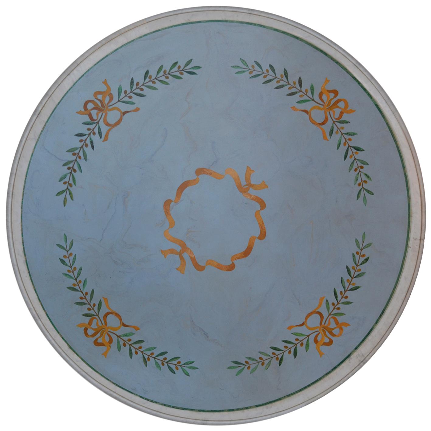 Adam style round dining or center table manufactured by hand in our laboratory of artists.
The round table top crafted in white carrara marble, displays a refined  scagliola inlay decoration  of green  olive branches joined by  gold yellow  ribbons