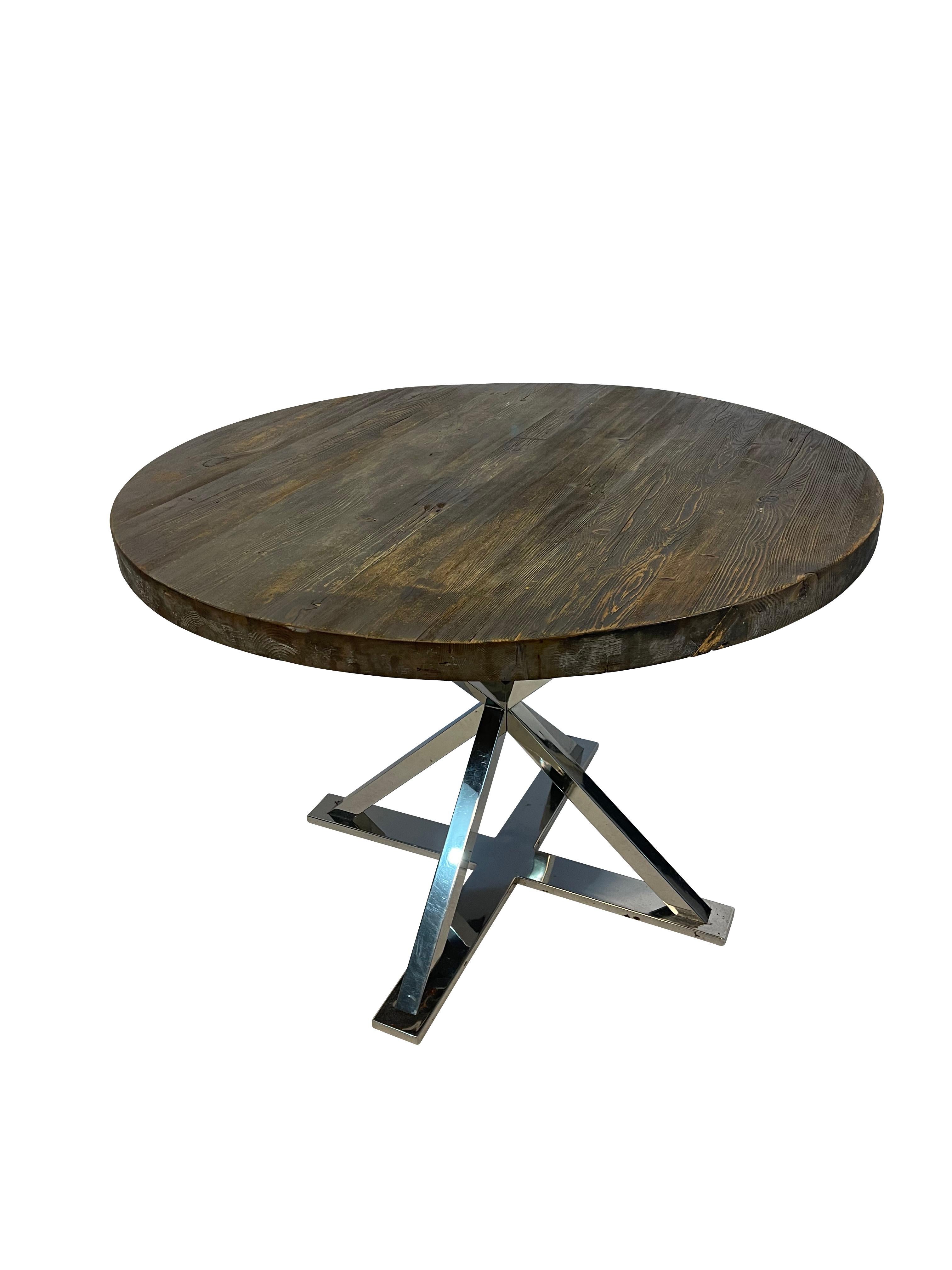 Rustic round farm table top with a modern chrome cross bar base.  The top appears to be reclaimed wood. A mix of the old and new,  Perfect in a modern or modern farmhouse setting as a kitchen, dining, or accent table. 