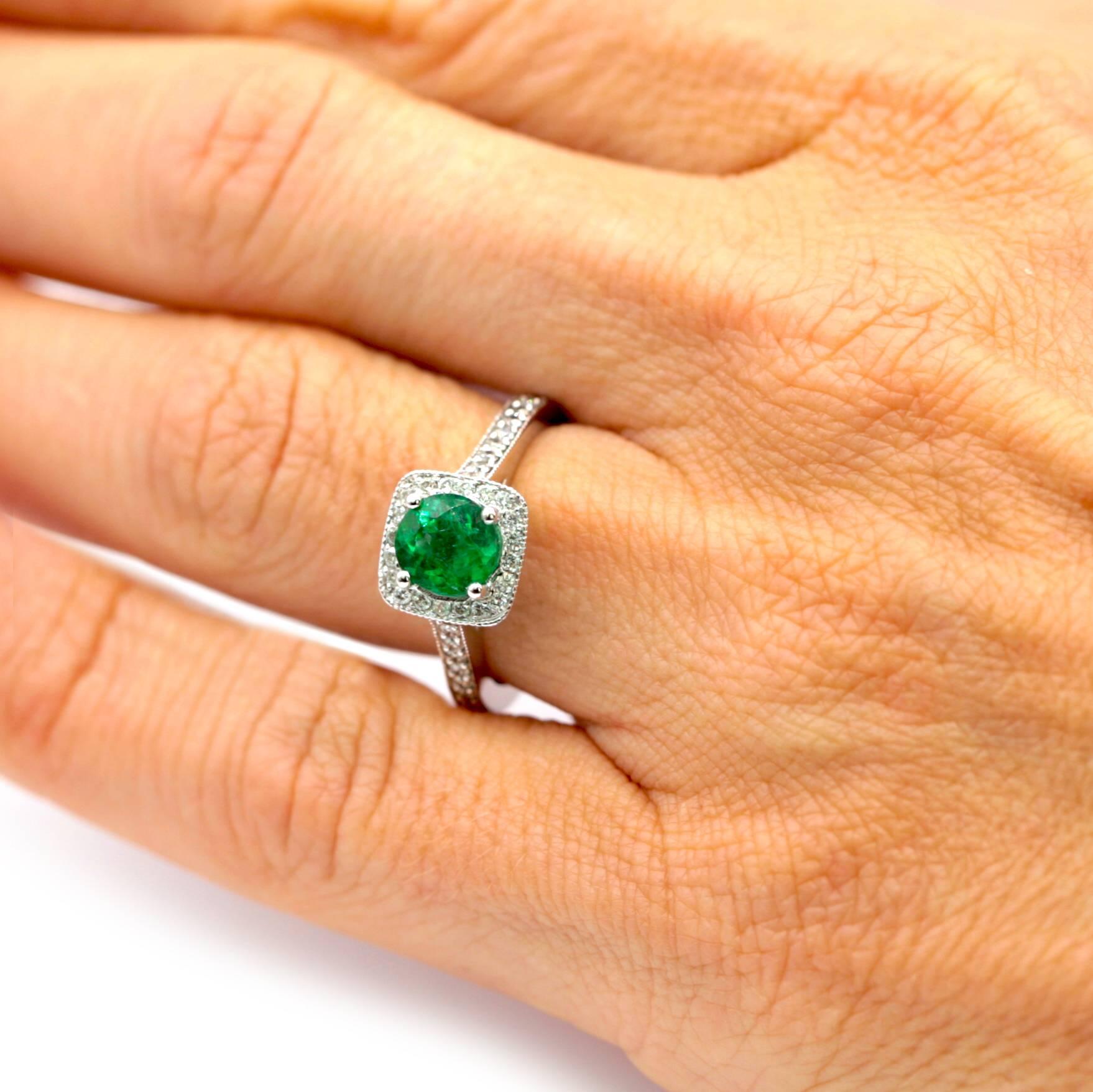 Round Green Emerald weighing 1.25 carats with a certificate from the American Gemological Laboratories stating that it is natural. The emerald is mounted in a fourteen karat white gold halo setting with twenty round diamonds. The shank of the ring