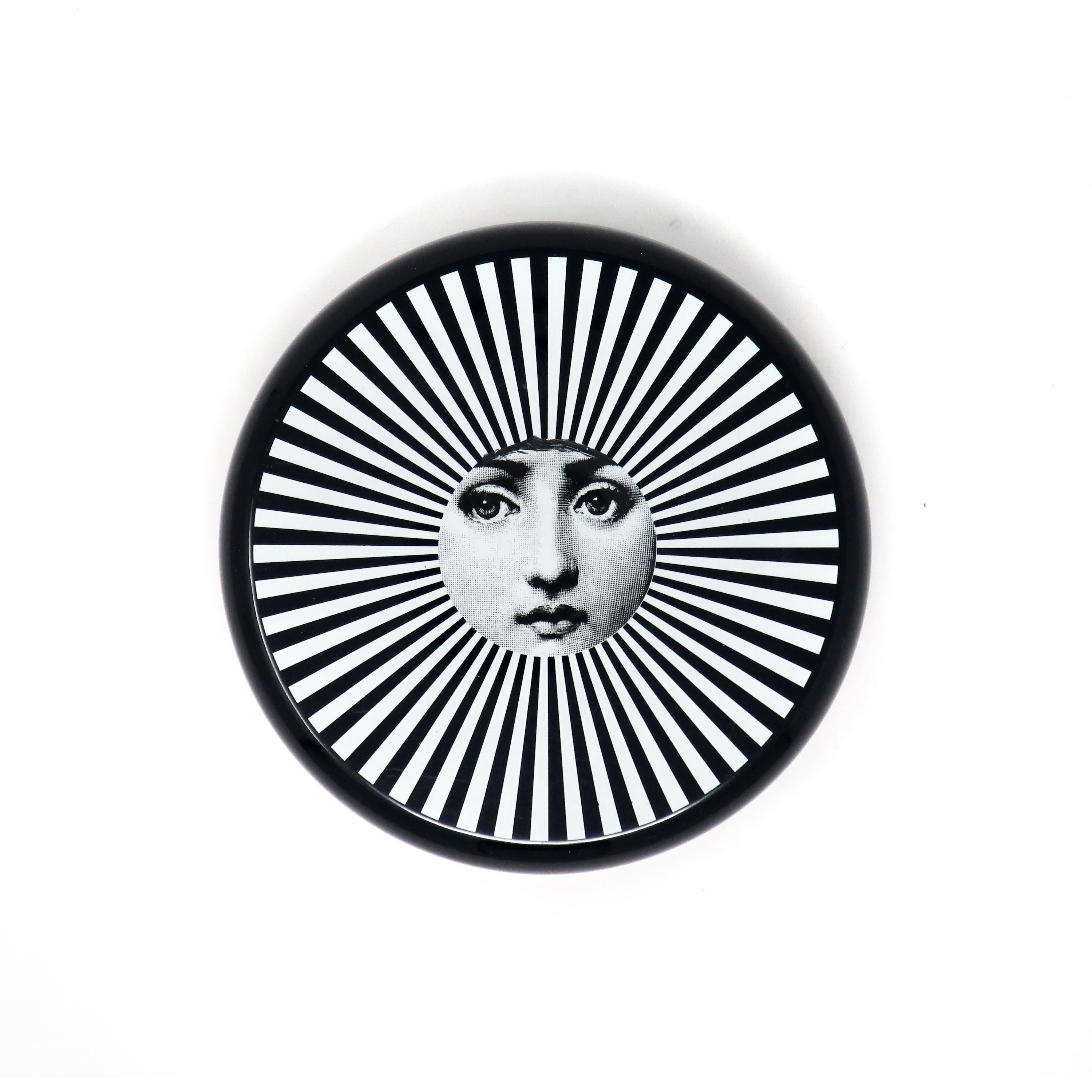 Beautifully crafted and lacquered, and lined in padded velvet, this round trinket box by Fornasetti will add a great decorative touch to your home. Features a whimsical sun design in black and white with a woman’s face in the center. Perfect for