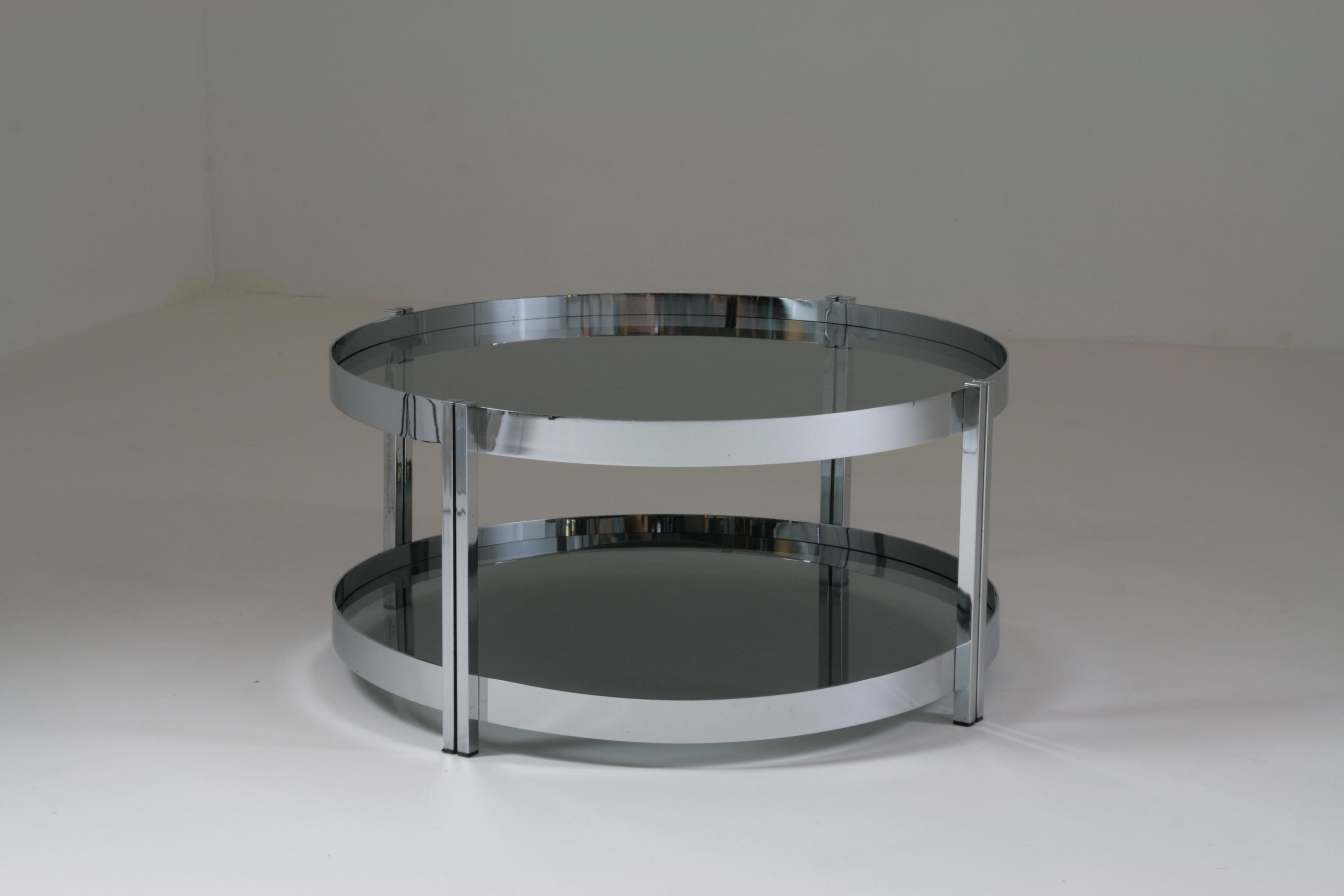 Table basse ronde en métal chromé fabriquée en France dans les années 1970. Les deux plateaux en verre fumé sont amovibles et sont très pratiques au quotidien pour le rangement ou l'insertion d'objets décoratifs. Quelques traces d'utilisation sur