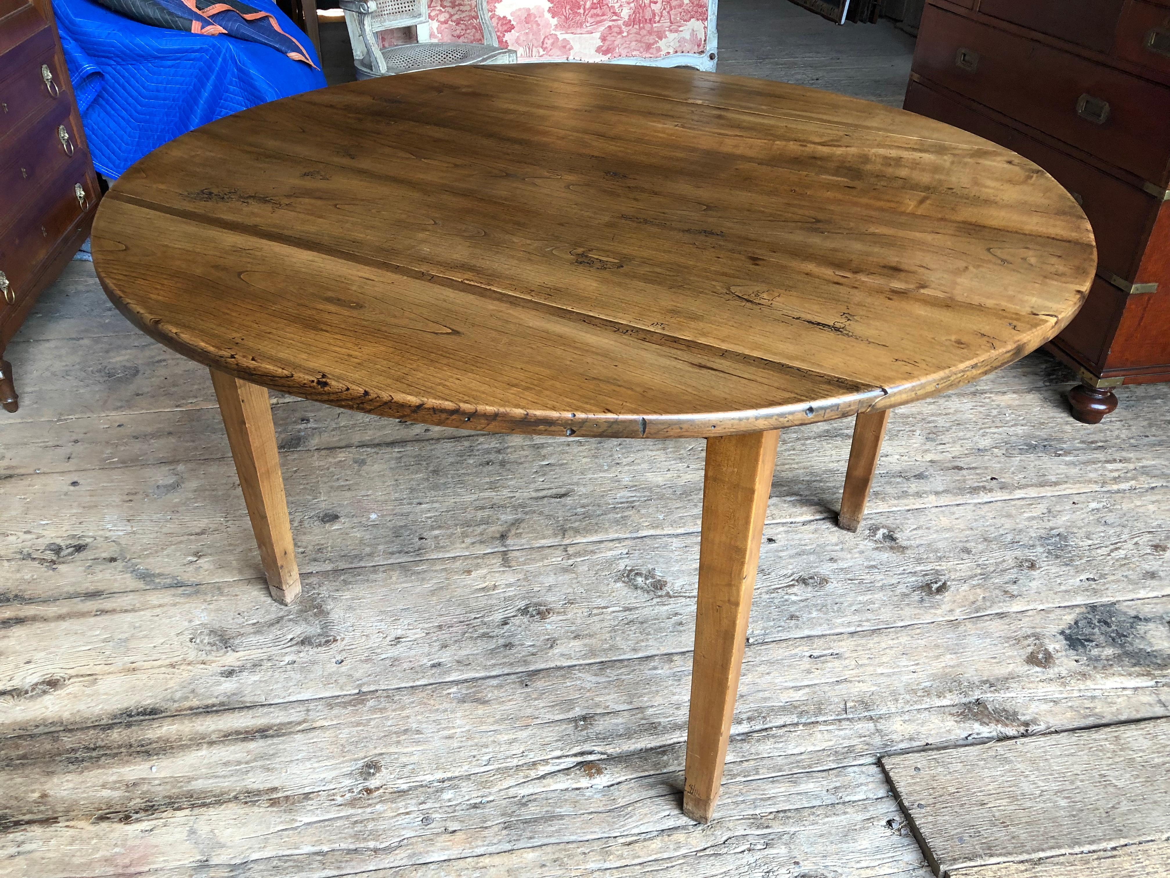 A French, mid-19th century, round drop-leaf farm table in light cherry, with simple tapered legs.
