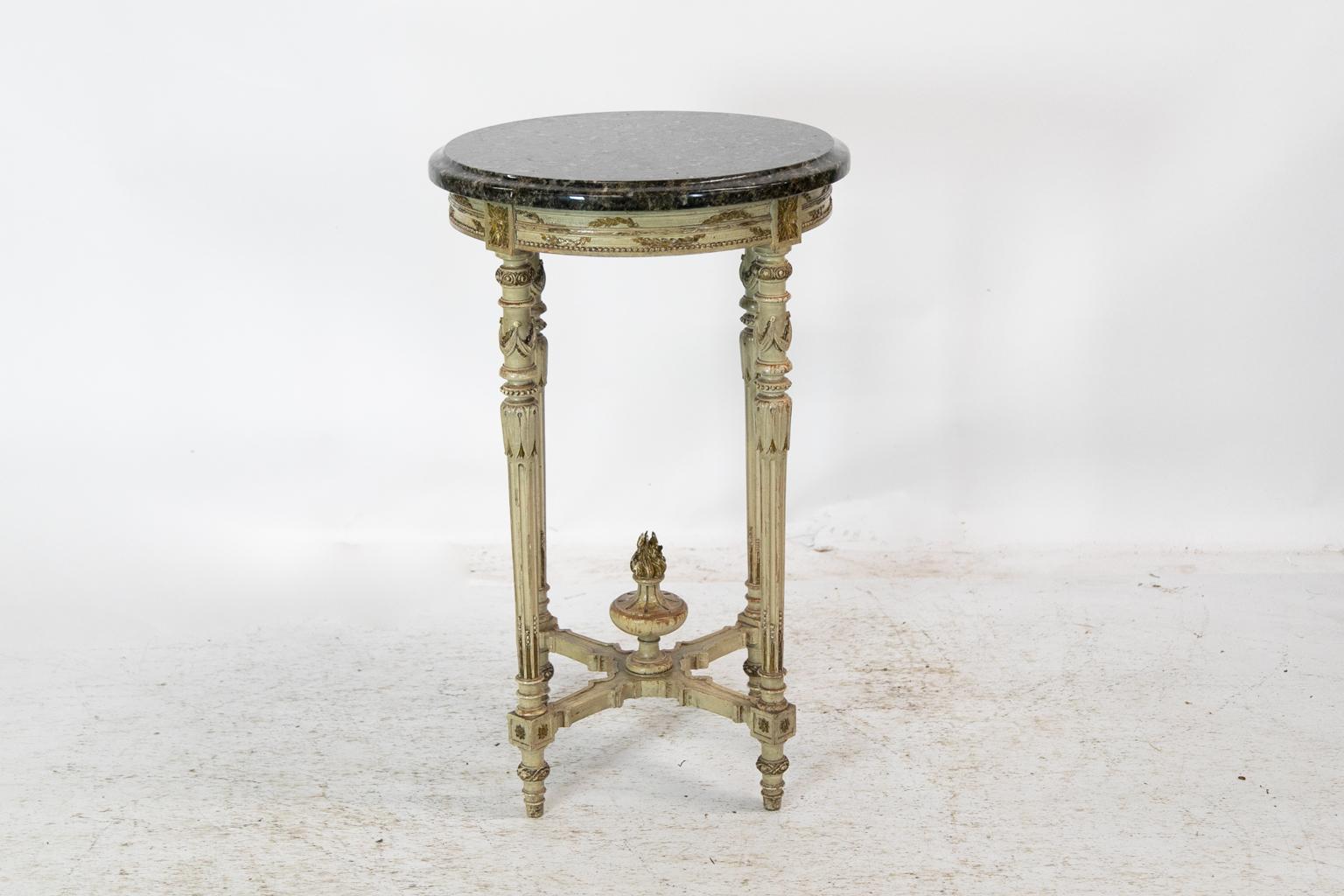 This occasional table has an apron with carved leaf swags and a repeating bead molding highlighted with gold. The legs have drapery swags carved in high relief. Below are carved stylized acanthus leaves and stop fluted legs. The legs are connected