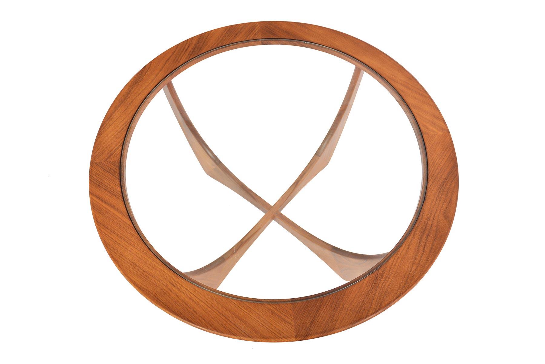 This iconic English Mid-Century Modern round teak afromosia and glass coffee table was designed by Victor Wilkins for G Plan’s Astro range in the 1960s. A round plate of glass is supported by beautifully sculpted banding and stands on parabolic