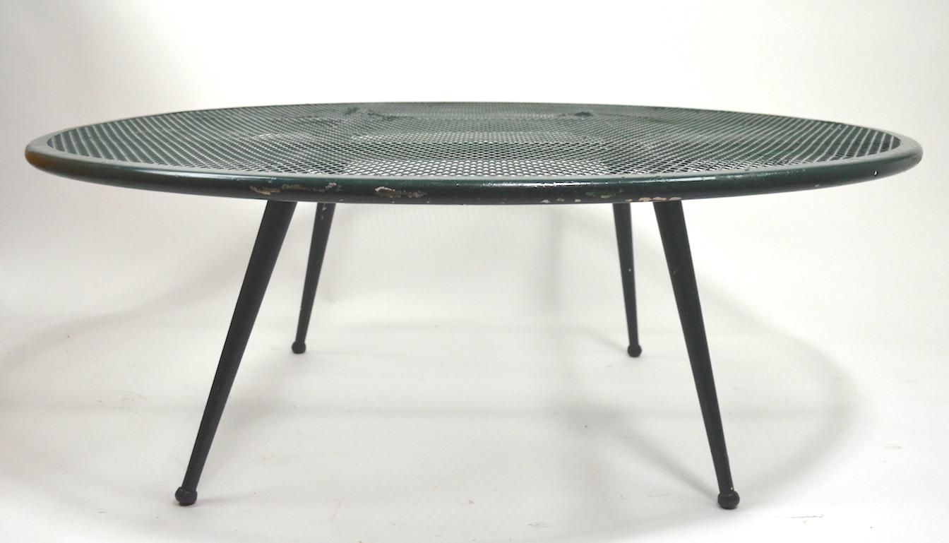 Stylish circular metal garden or patio table attributed to Woodard. This table has a metal mesh top with splayed tapered pole legs. Currently in green paint finish which shows some wear, usable as is, or we offer custom powder coating if you prefer