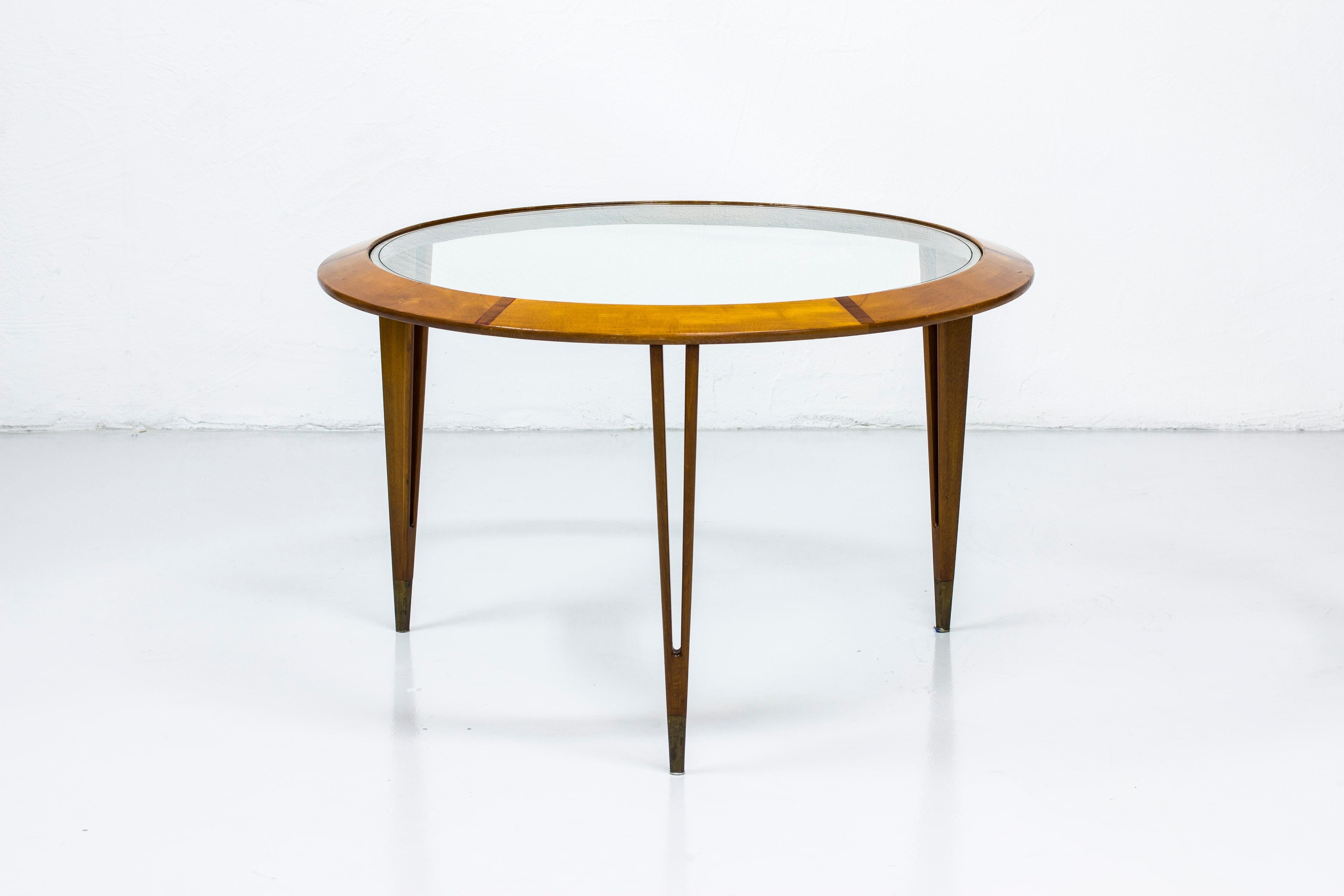 Round coffee table designed by Bertil Fridhagen. Produced in Sweden by Bodafors during the 1940s-1950s. Made from beech wood with contrasting inlays of mahogany in the circular frame. Glass top with etched line. Tapered legs with brass feet endings.