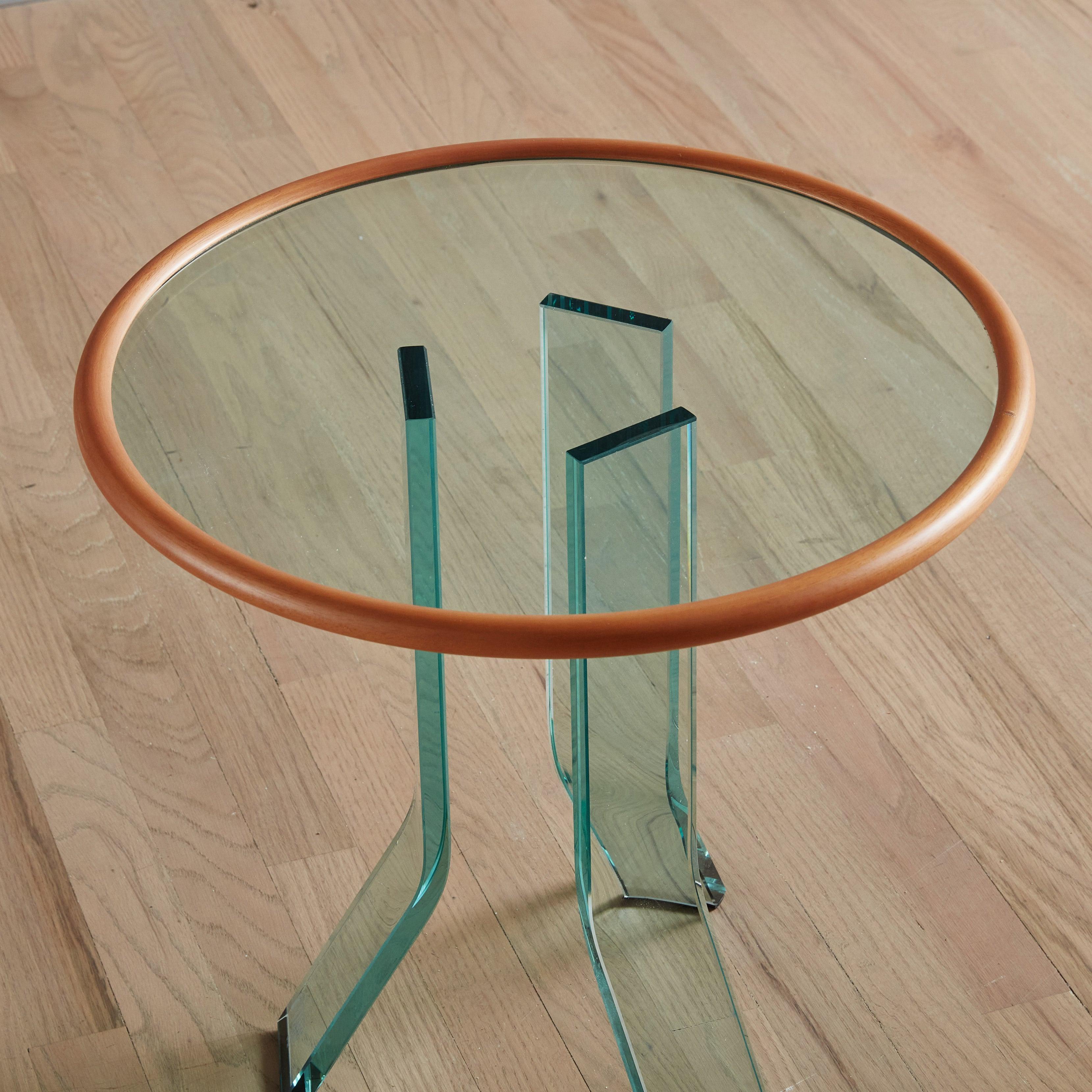 A Postmodern round side table designed by Italian glassmaker FIAM in the 1980s. This side table features an aqua hued, circular glass top with contrasting blonde wood trim. Three rectangular, angled glass legs support the top and give this piece a