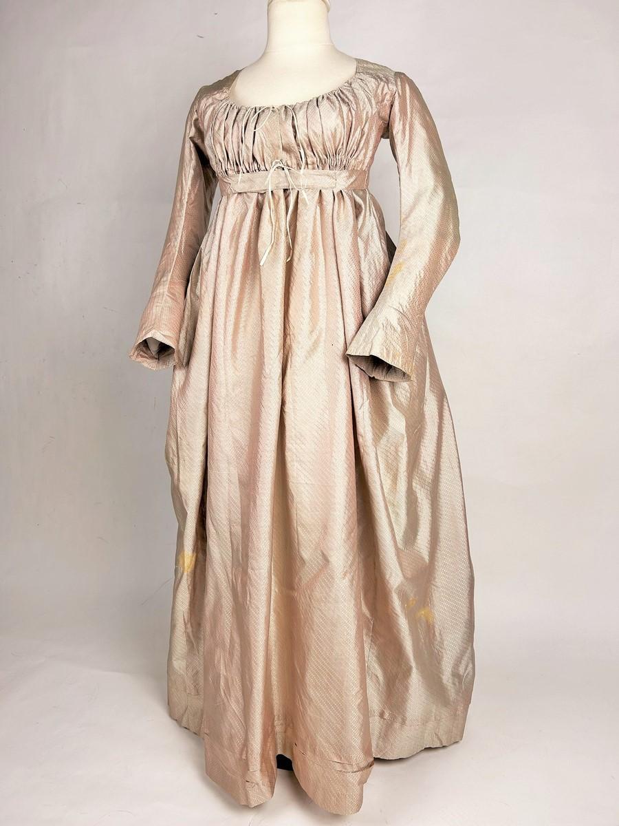 Circa 1792-1795
Francia
Abito a vita alta in seta rosa salmone con semi geometrici risalente alla Prima Repubblica Francese. Bustier con ampio scollo ovale finemente stretto sul busto da lacci scorrevoli originali. Maniche lunghe e angolate con