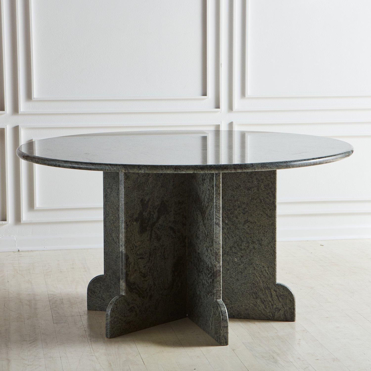 A vintage dining table constructed with green granite featuring a 1” thick round tabletop, which sits on a unique base with curved feet. The base consists of three separate sections. Each section is made with two granite slabs. USA, 20th century.