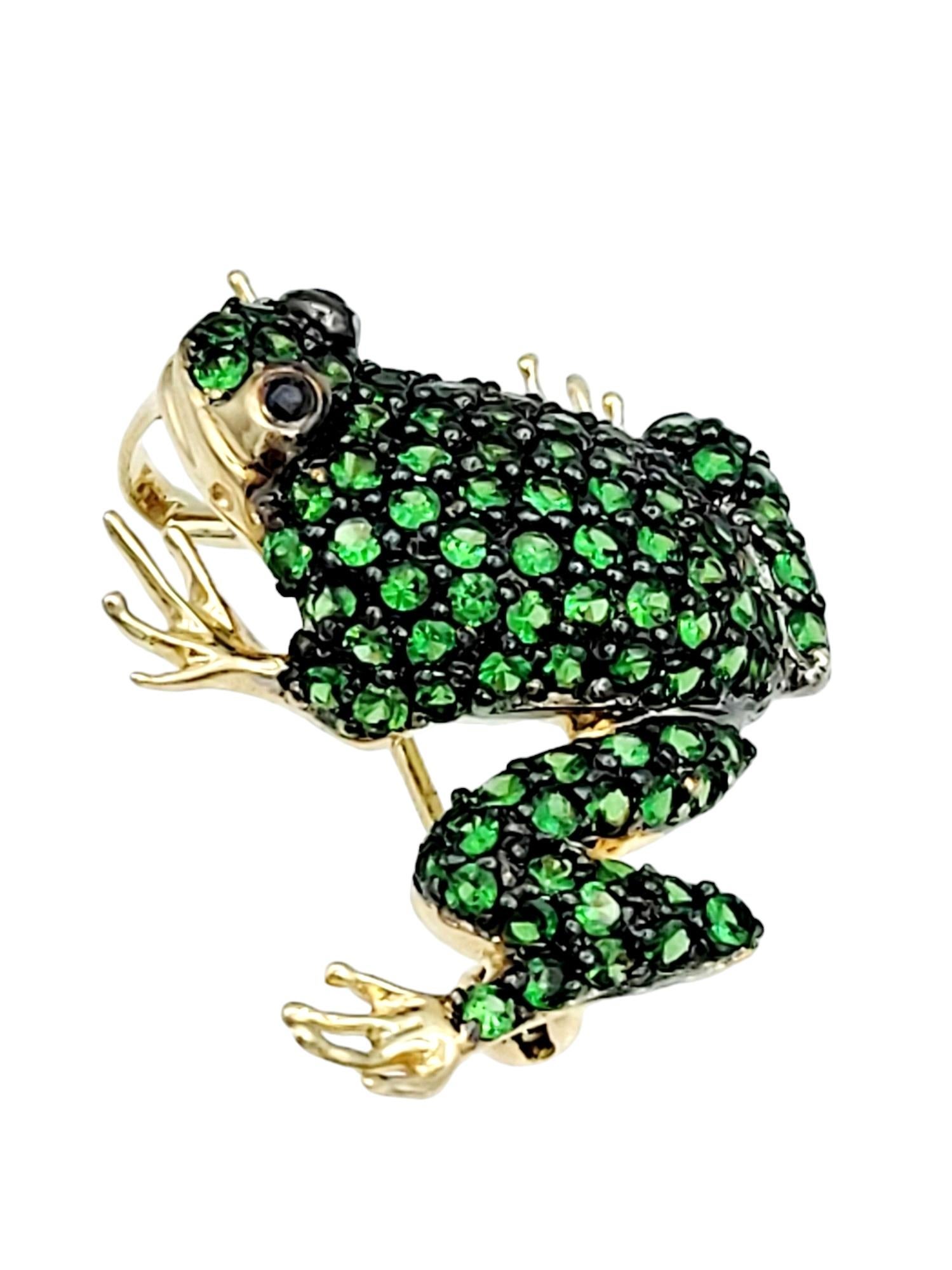 This frog brooch, set in radiant 14 karat yellow gold, is a whimsical and charming piece of jewelry. The body of the frog is adorned with vibrant green tsavorite stones, creating a lively and eye-catching display. The use of tsavorite stones adds a