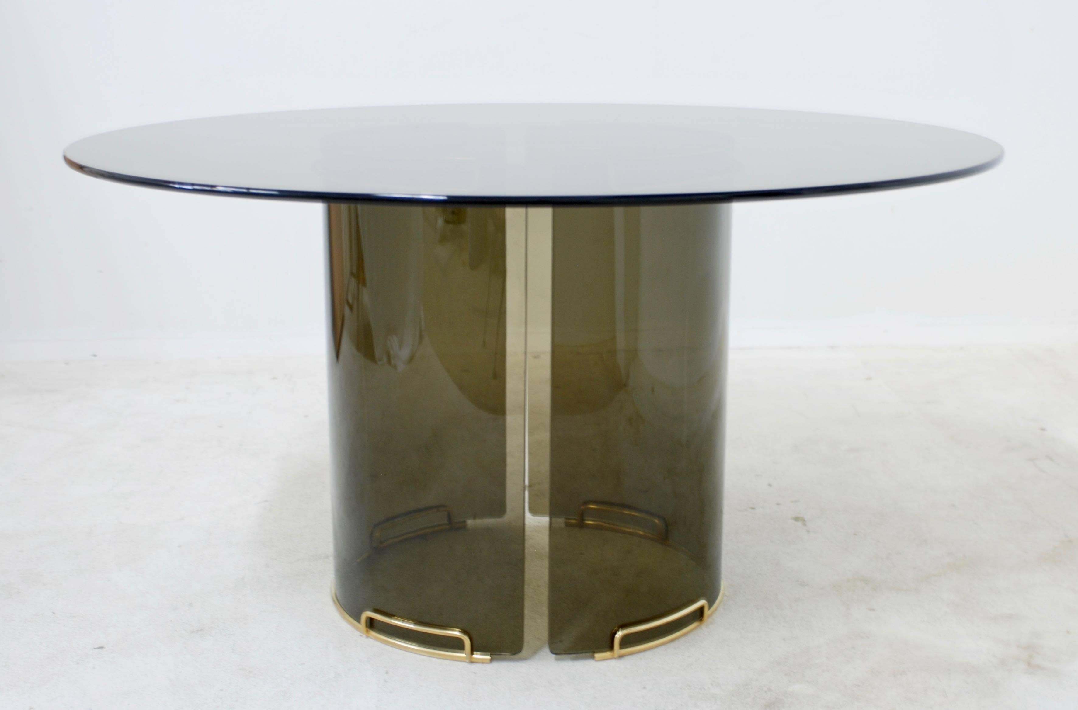 An Italian style 1970s round smoky gray glass dining table which could possibly be the work of Fontana Arte. The base is made of two pieces of curved glass that have chic brass fittings on the base and top. The bases measure 28.25