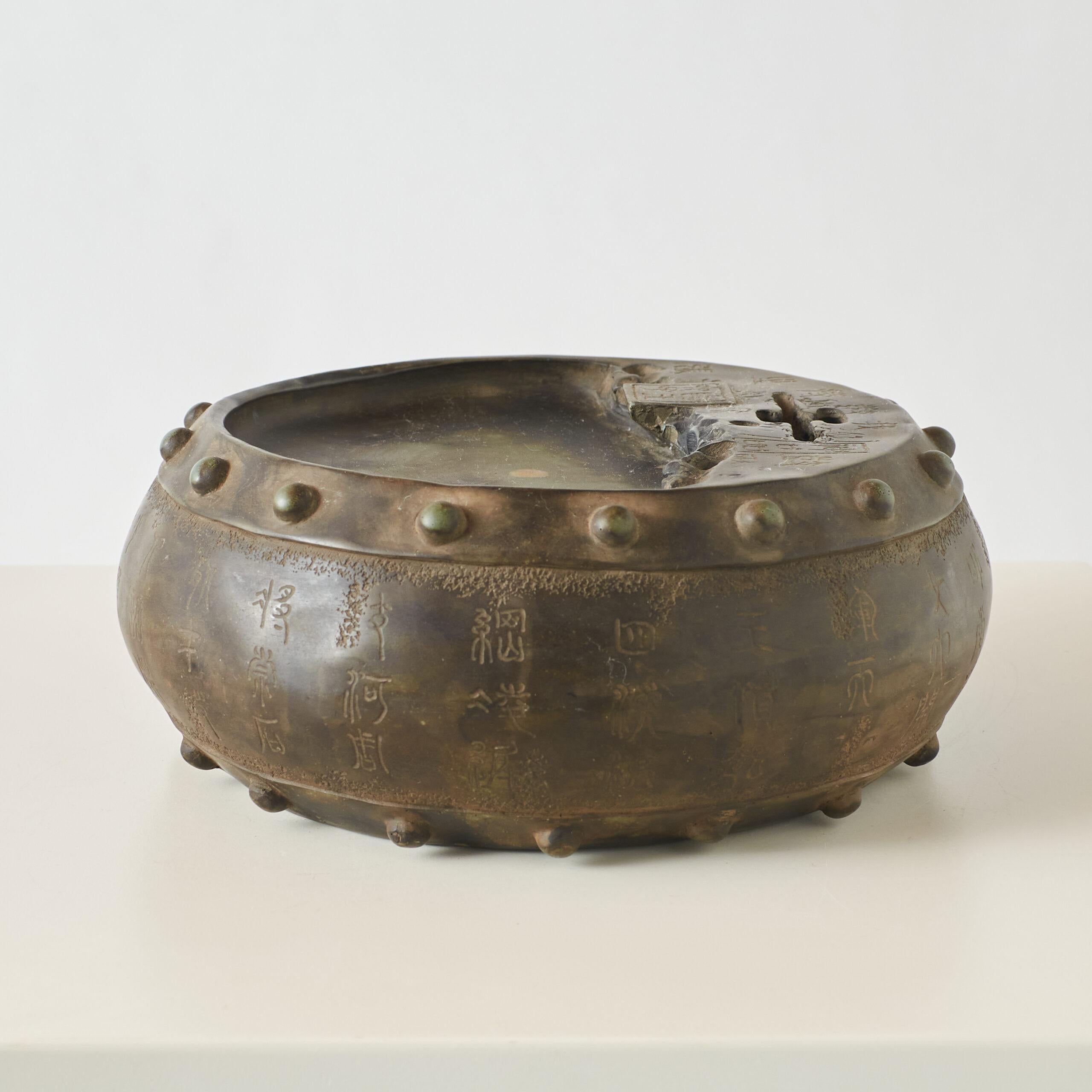 Runder Tintenstein mit Qianlong-Marke

Ein runder chinesischer Tintenstein mit einer dunklen, strukturierten Außenseite und einer glatten zentralen Mulde zum Zerreiben von Tinte. Der Rand ist mit erhabenen kreisförmigen Motiven verziert. Die
