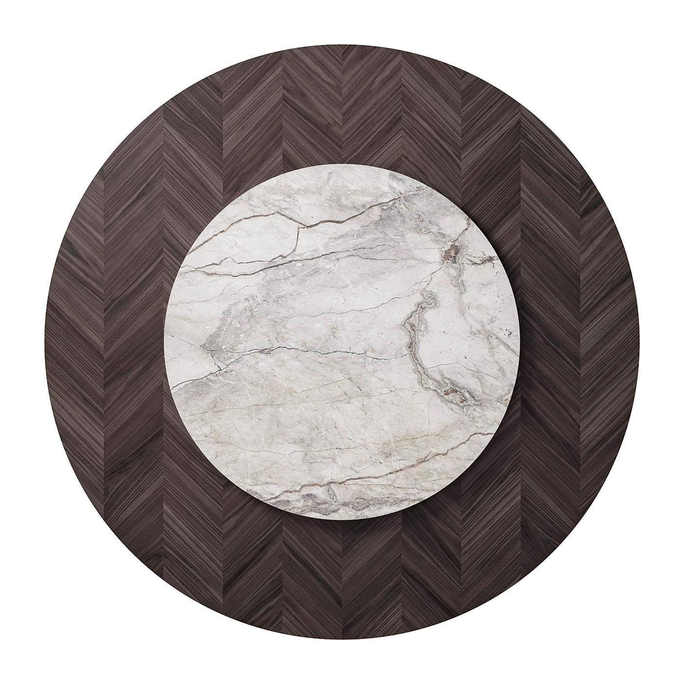 From a wide collection of tables by Cipriani, the round inlaid dining table features a chic top in Hungarian herringbone veneer, transmitting a sense of timeless style and luxury. Standing on a round metal plate that echoes the table's surface, the