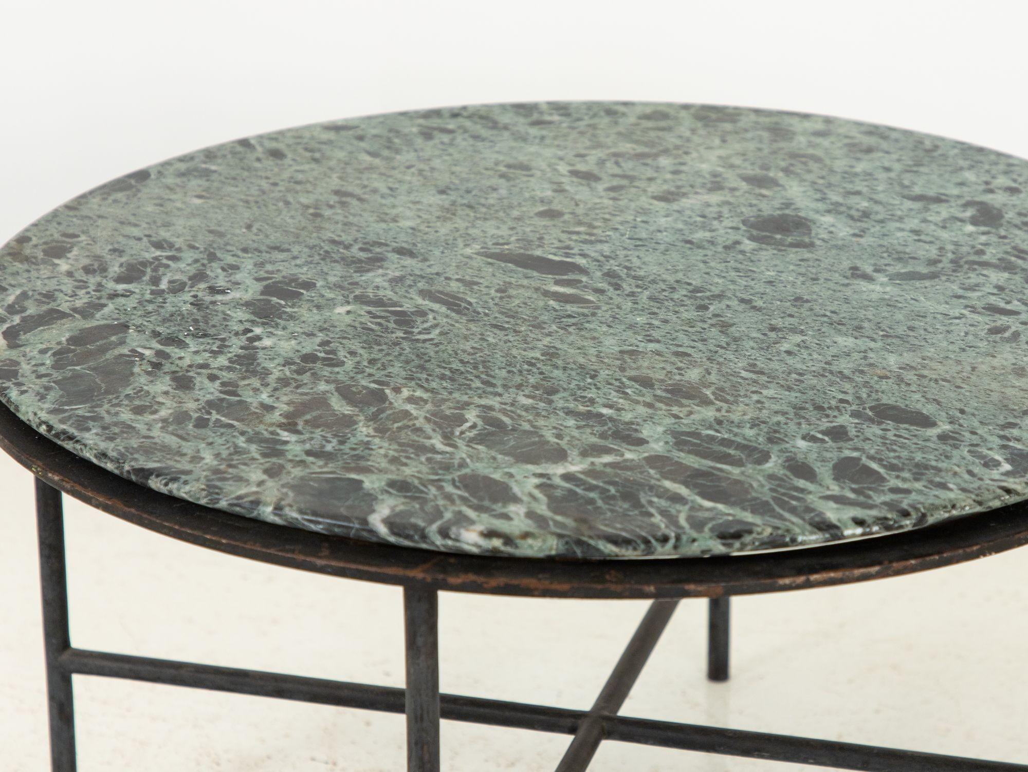De la tapisserie vibrante du design des années 1960, en France, émerge une captivante table à cocktail ronde à base de fer, couronnée d'un resplendissant plateau de marbre vert. La juxtaposition du fer industriel robuste avec l'allure riche et