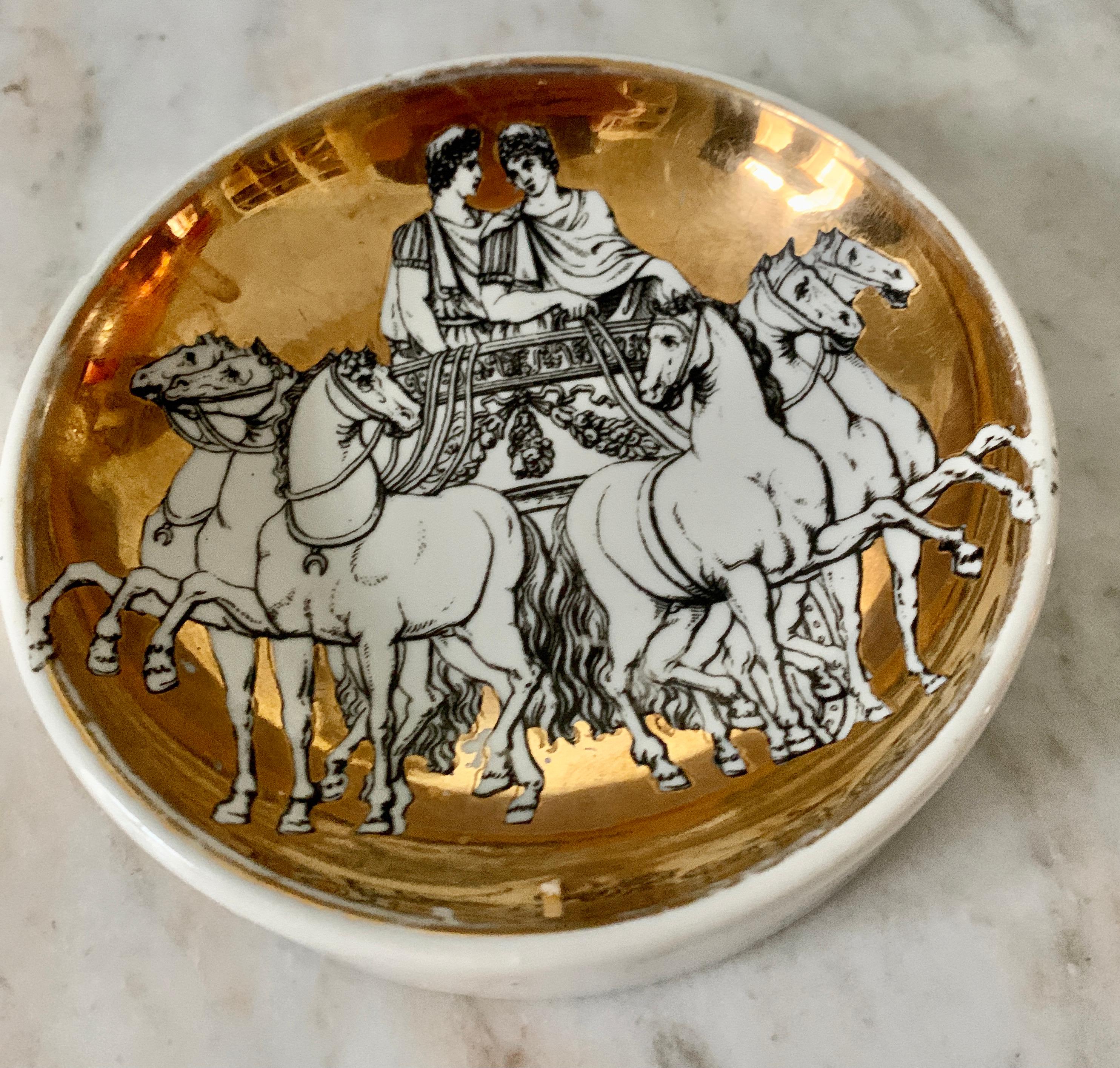 A wonderful gilt porcelain dish by Italian Designer Piero Fornasetti. The image is of two gay Roman soldiers being paraded through Rome in a Chariot Pulled by Horses. A dynamic image, and a compliment to any cocktail table as a decorative item or