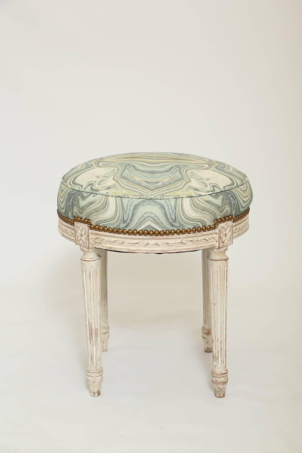 Ottoman, having a round, crown seat with nailheads, on a painted frame, with natural wear, its apron carved with ribbons and rosettes, raised on round, tapering, fluted legs, ending in touipe feet. 

Stock ID: D1485.