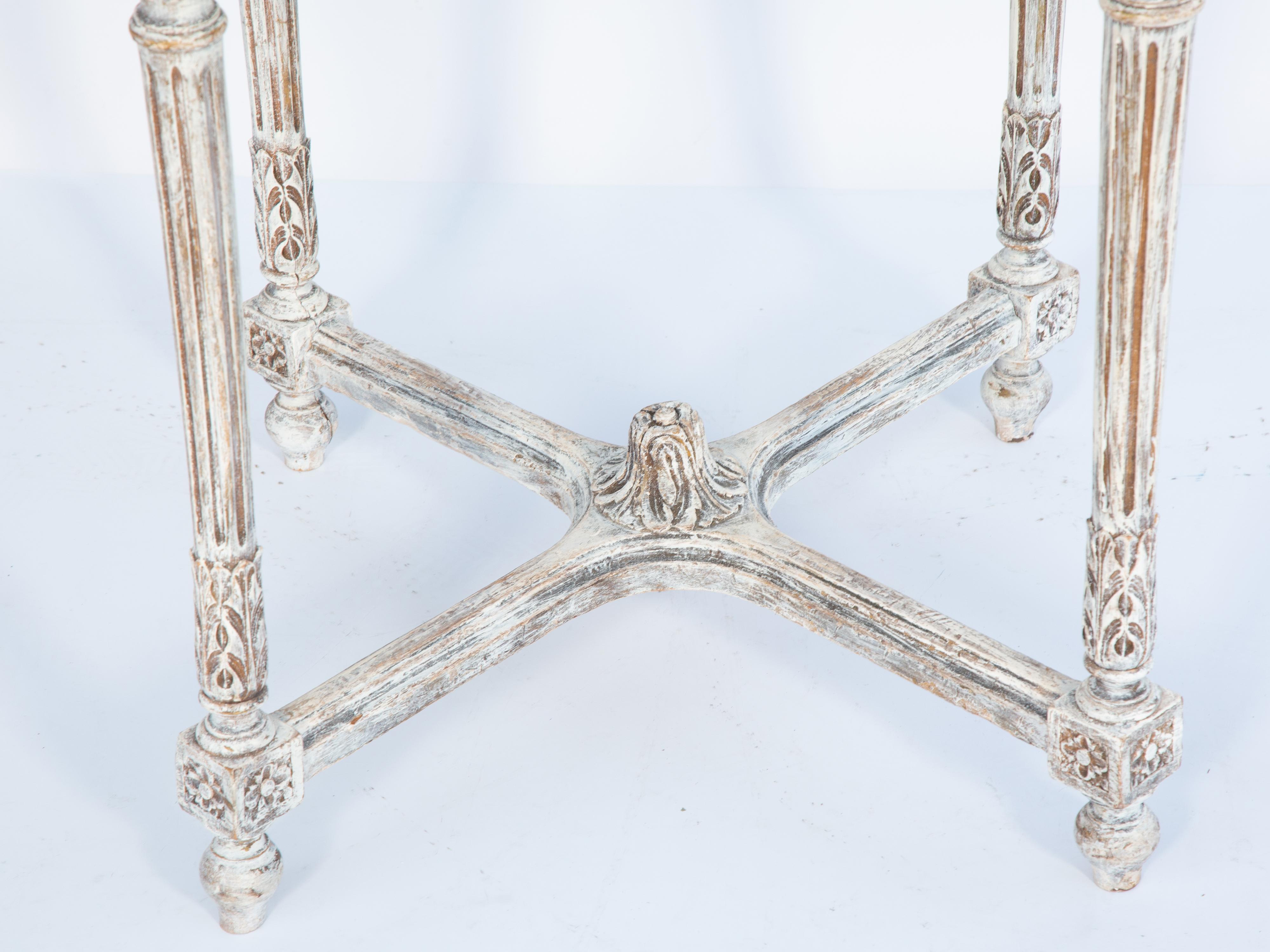 Occasional table having a painted finish showing natural wear, with a round top of antiqued mirrorplate, its gadrooned border over round guilloche apron, raised on rosette-headed, round, tapering, fluted legs, joined by X-stretcher, ending in toupie