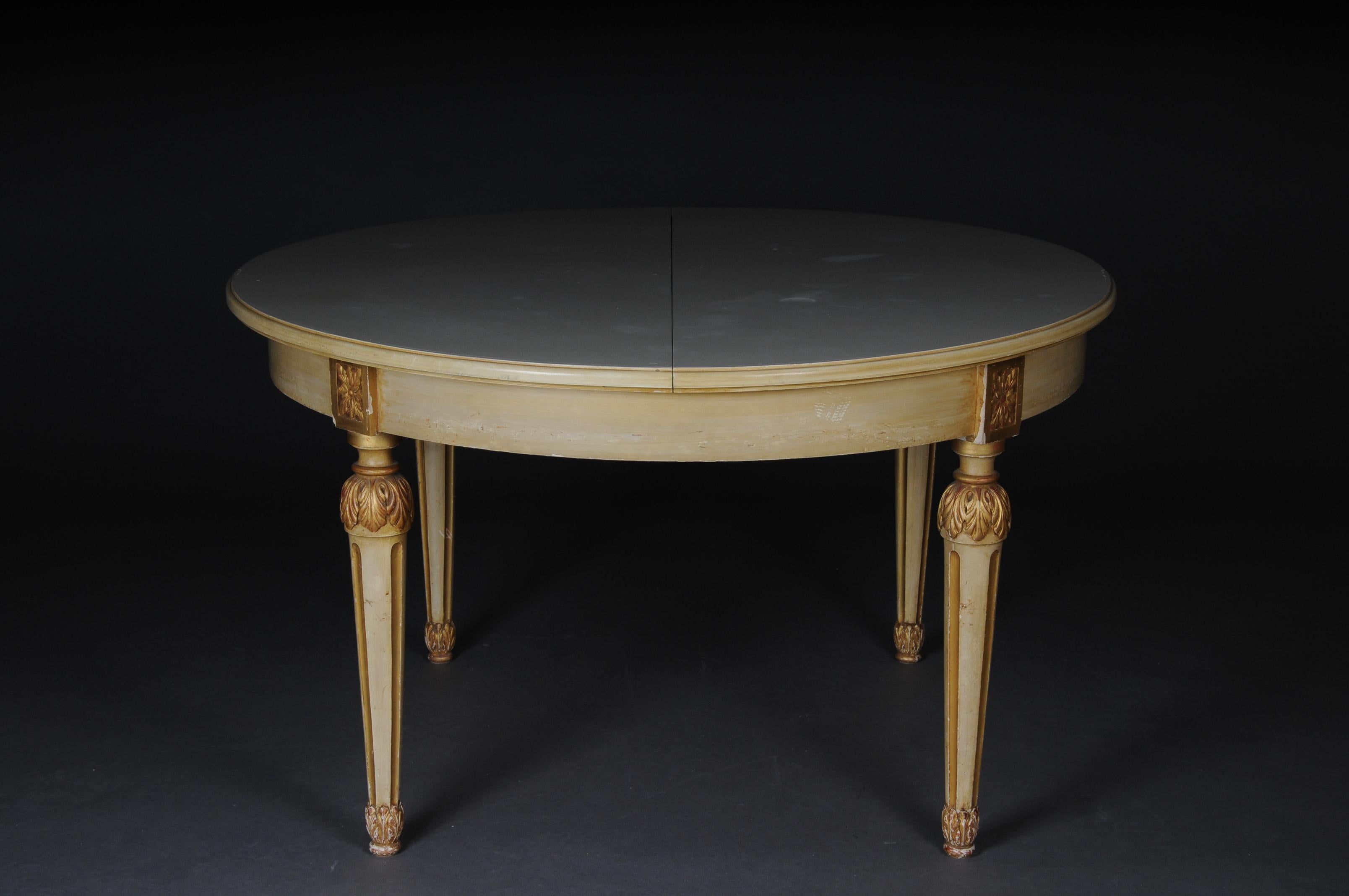 Round lounge dining table Louis XVI, circa 1930.

Solid wood, cream-framed and partially gold-plated table in Louis XVI style. Round plate on tall, conical, fluted pointed legs.
Extendable table with integrated tops.

Please take the condition