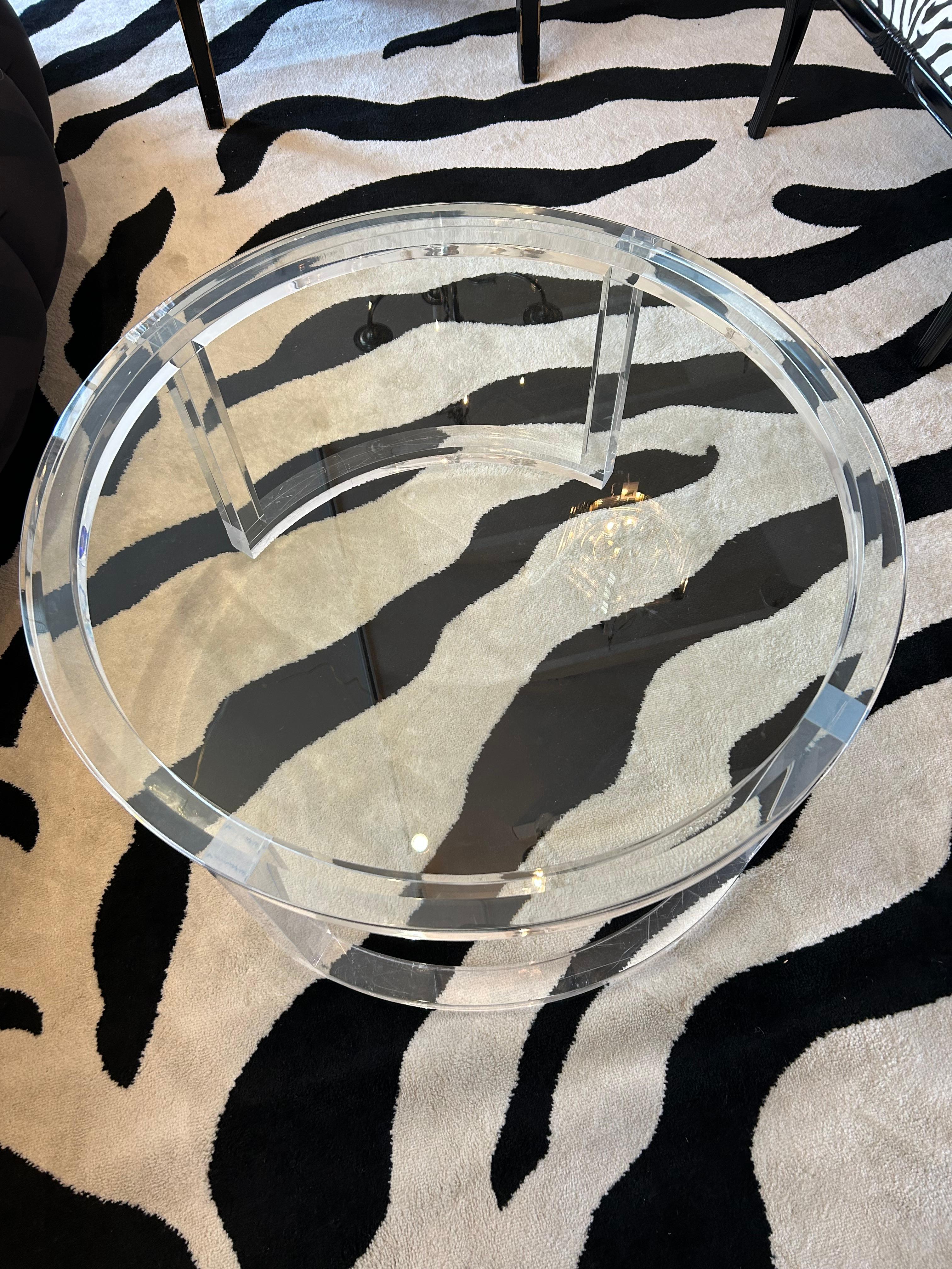 Table basse ronde et élégante avec base en lucite et plateau en verre trempé biseauté.