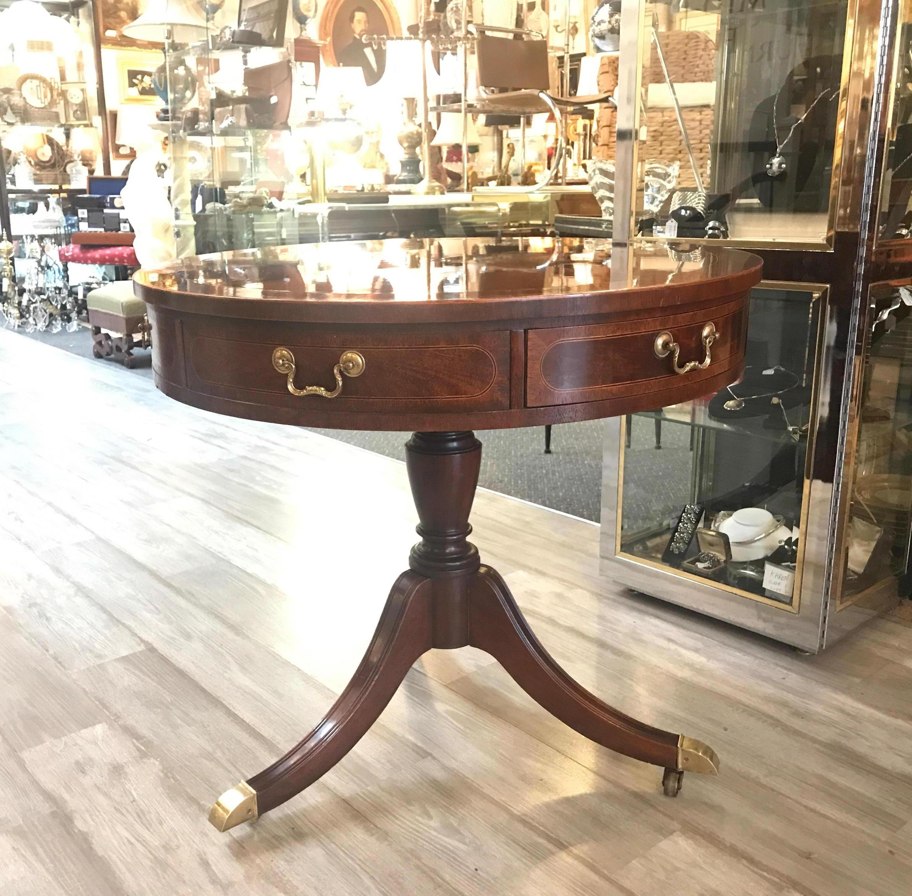 Beautiful Baker quality round mahogany drawered table with banded edge. The flame mahogany top with ewe wood band with drawer fronts all around the apron. Two drawers are working drawers. The top is supported buy a turned central column with triple