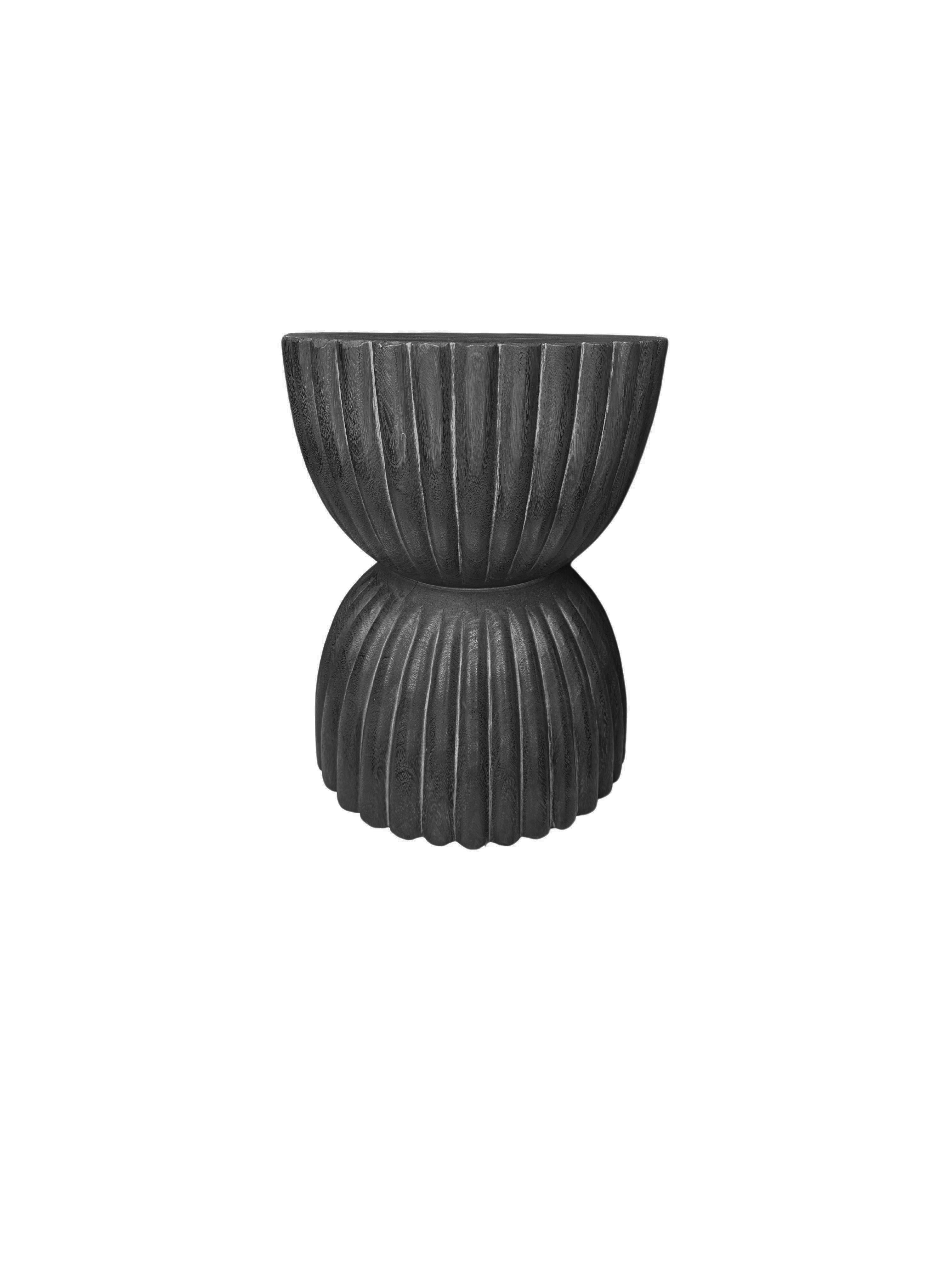 A wonderfully sculpted side table, crafted from a single block of mango wood. It features wonderful wood textures. This table features carved detailing that wraps around its sides. To achieve its black finish the wood was burnt several times and
