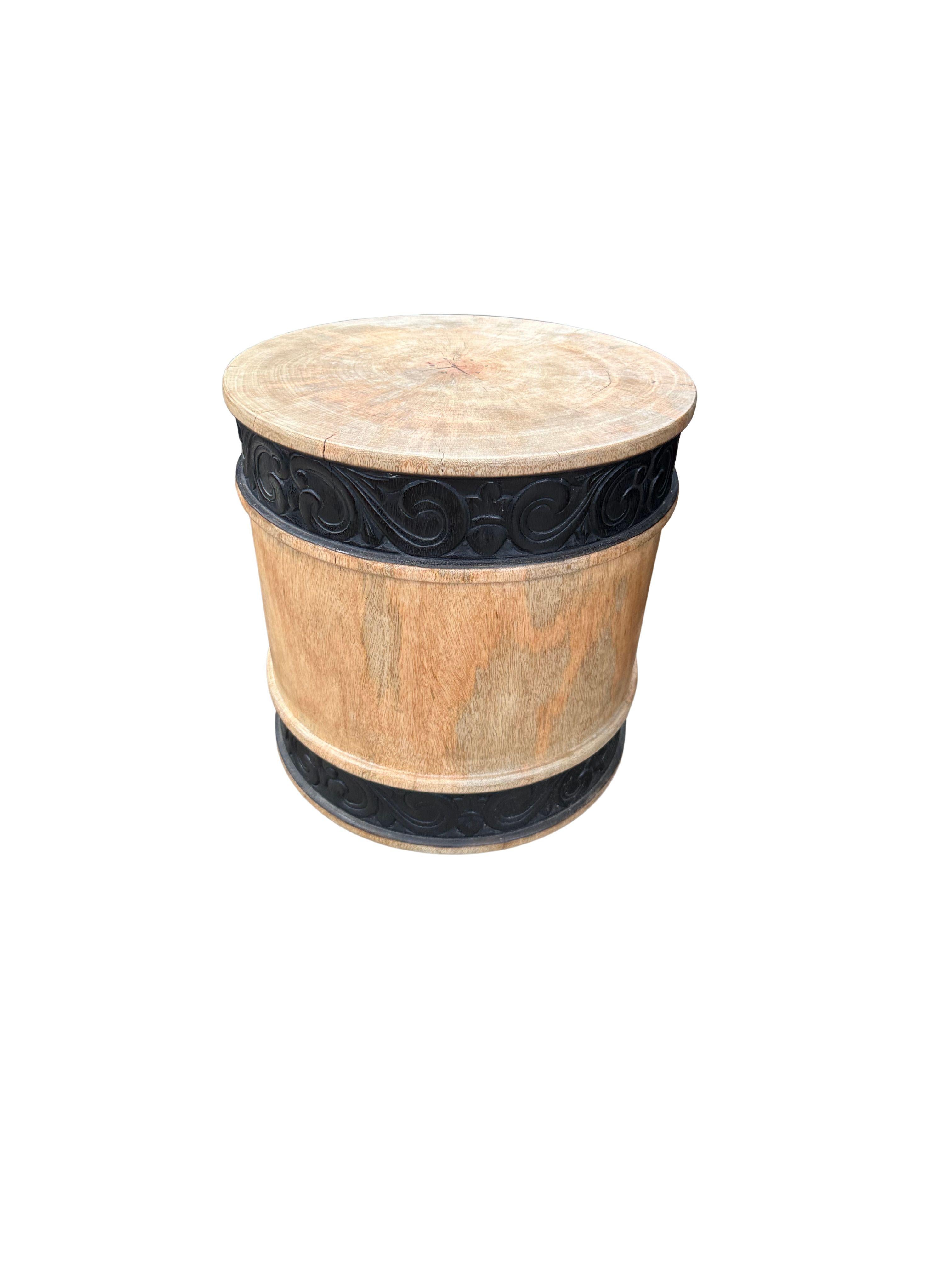 A wonderfully sculpted side table, crafted from a single block of mango wood. It features wonderful wood textures. The item was sanded and smoothed allowing for a natural finish. This table features carved detailing that wraps around its base and