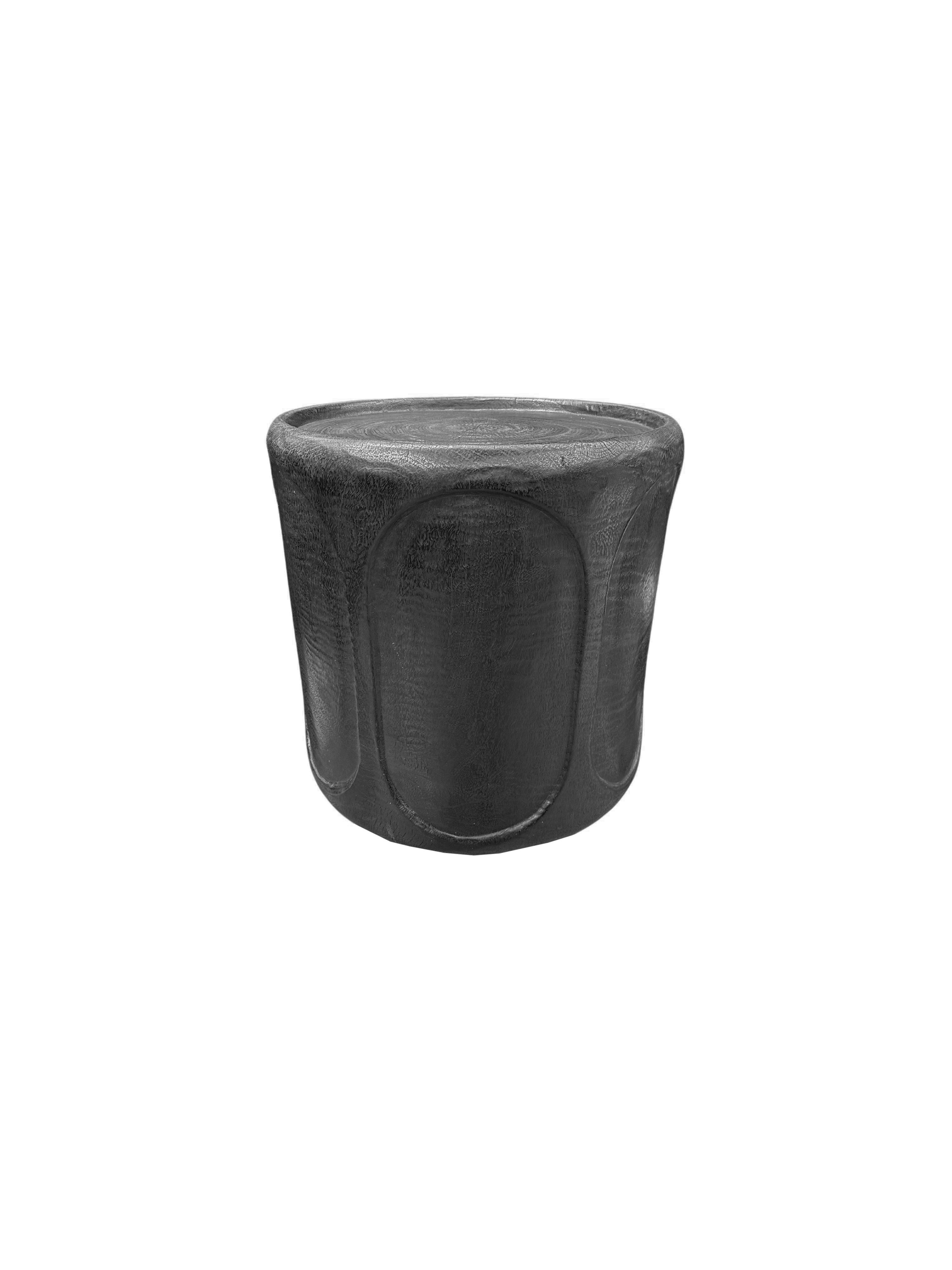 A wonderfully sculpted side table, crafted from a single block of mango wood. It features wonderful wood textures. This table features carved detailing that wraps around its sides. To achieve its black pigment the wood was burnt several times and