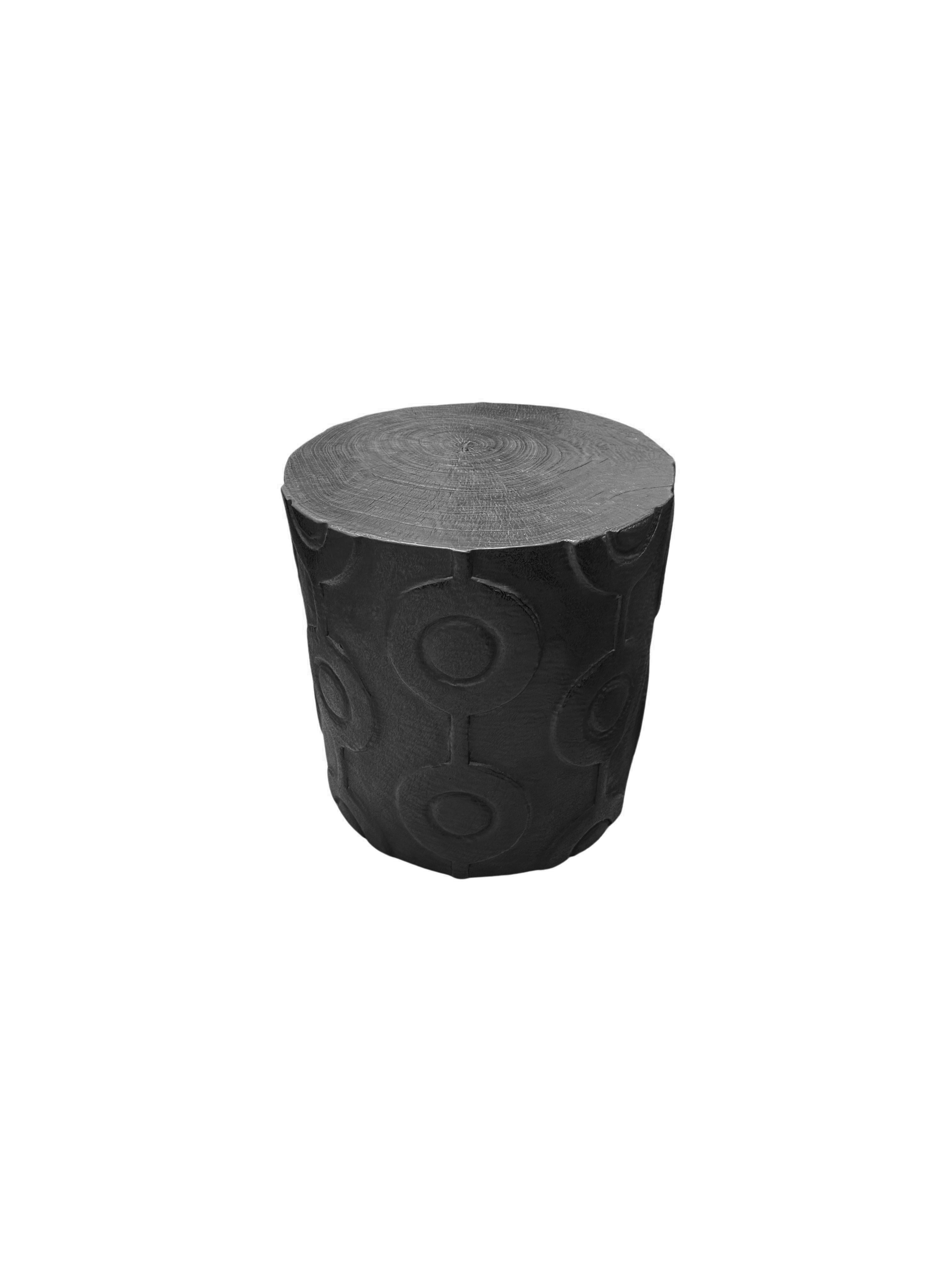 A wonderfully sculpted side table, crafted from a single block of mango wood. It features wonderful wood textures. This table features carved detailing that wraps around its sides. To achieve its black pigment the wood was burnt several times and