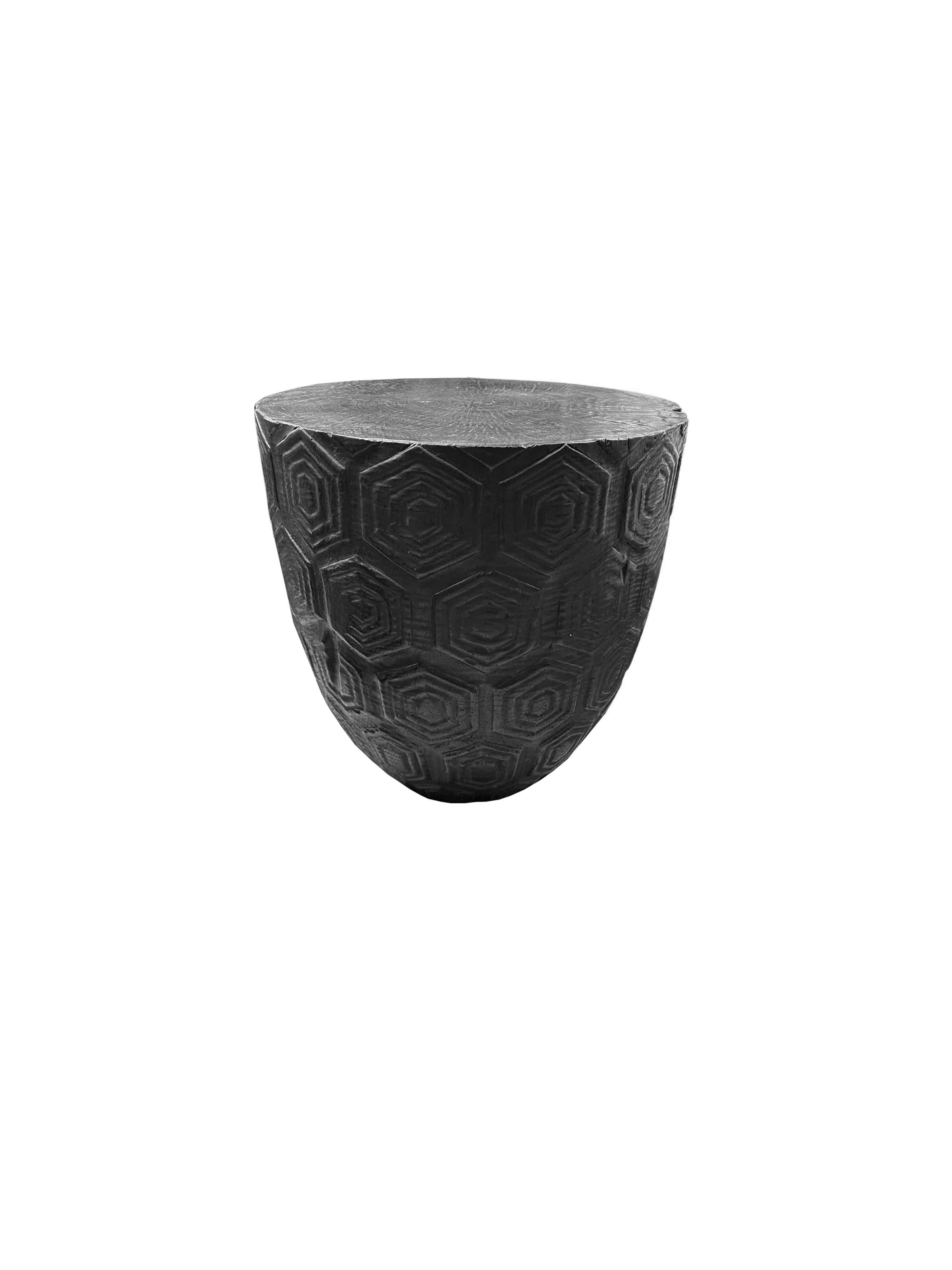 A wonderfully sculpted side table, crafted from a single block of mango wood. It features wonderful wood textures. This table features carved detailing that wraps around its sides. To achieve its black pigment the wood was burnt several times and