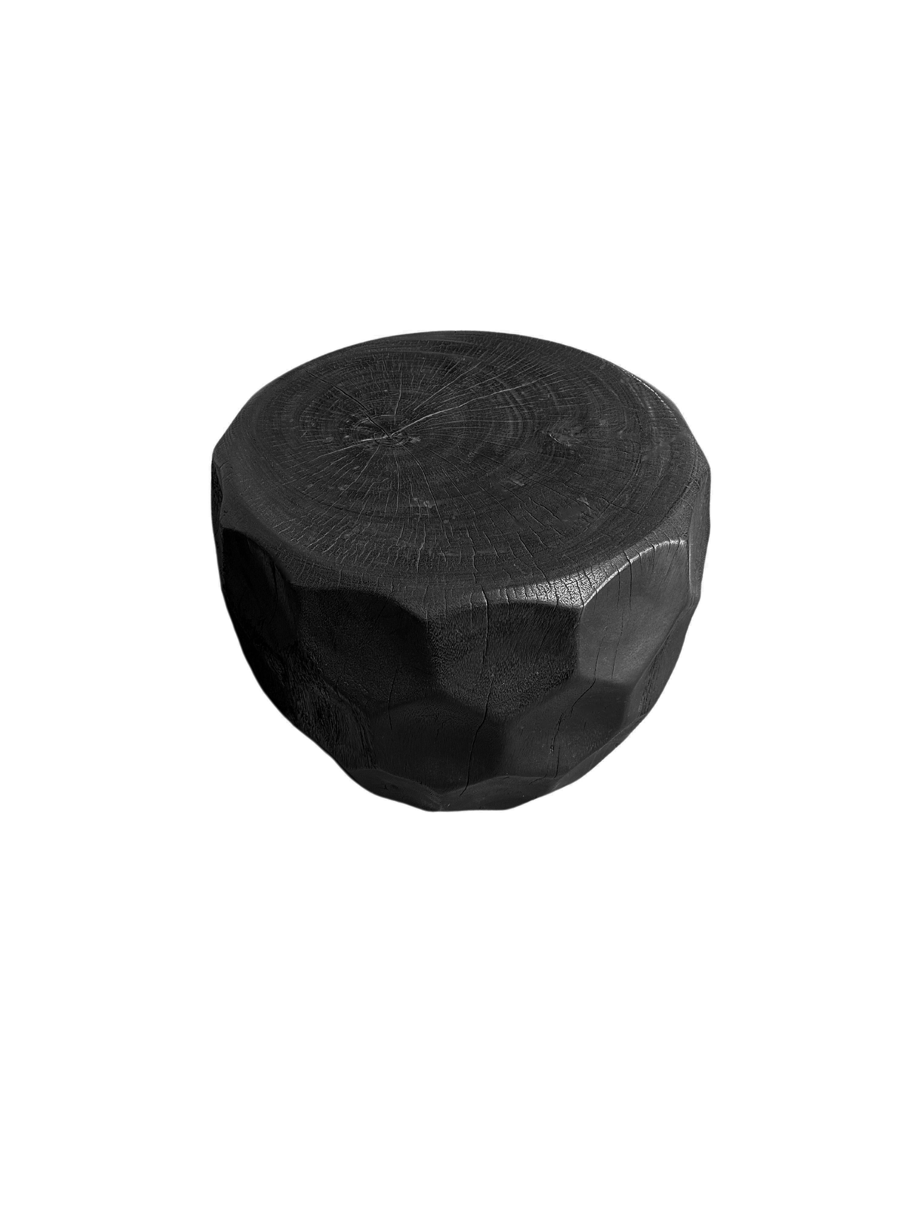 A wonderfully sculpted side table, crafted from a single block of mango wood. It features wonderful wood textures. This table features carved detailing that wraps around its sides. To achieve its black pigment the wood was burnt several times and