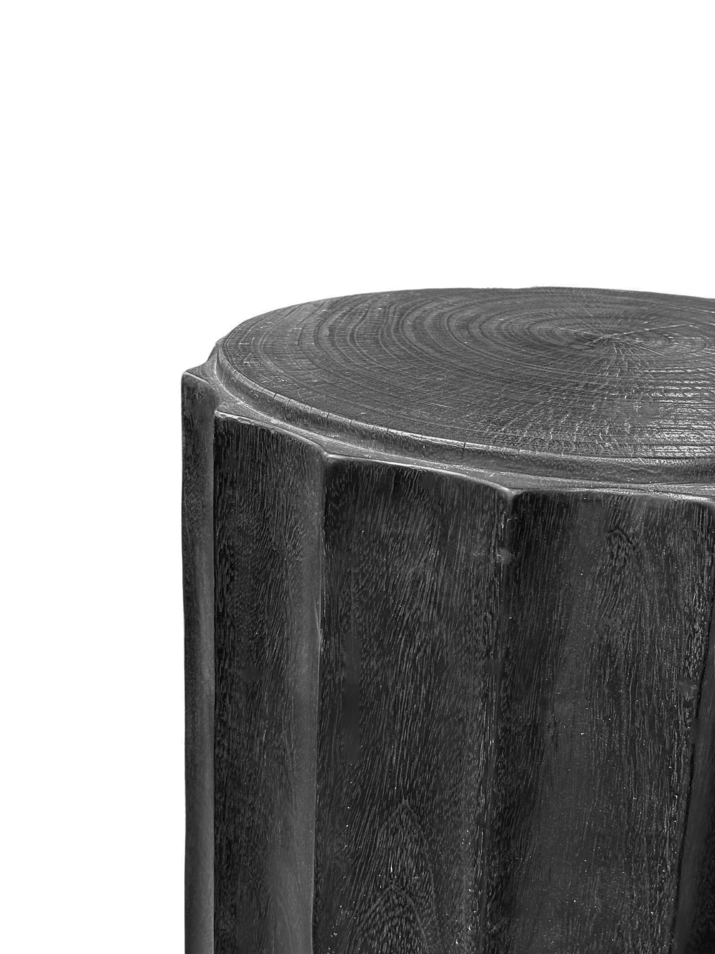 A wonderfully sculpted side table, crafted from a single block of mango wood. It features wonderful wood textures. This table features carved detailing that wraps around its sides. To achieve its black pigment the wood was burnt several times and