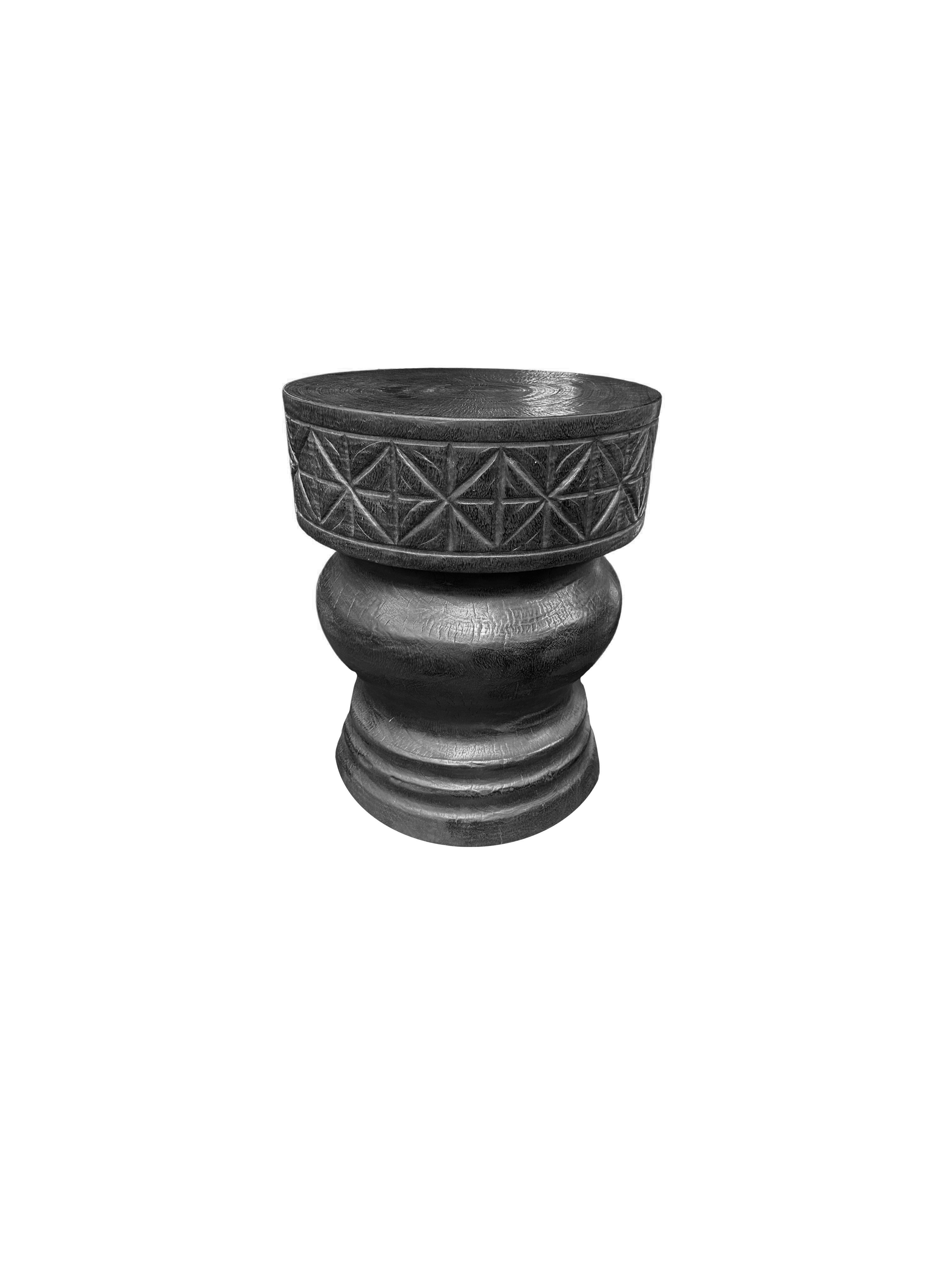 A wonderfully sculpted side table, crafted from a single block of mango wood. It features wonderful wood textures. This table features carved detailing that wraps around its sides. To achieve its black pigment the wood was burnt several times and