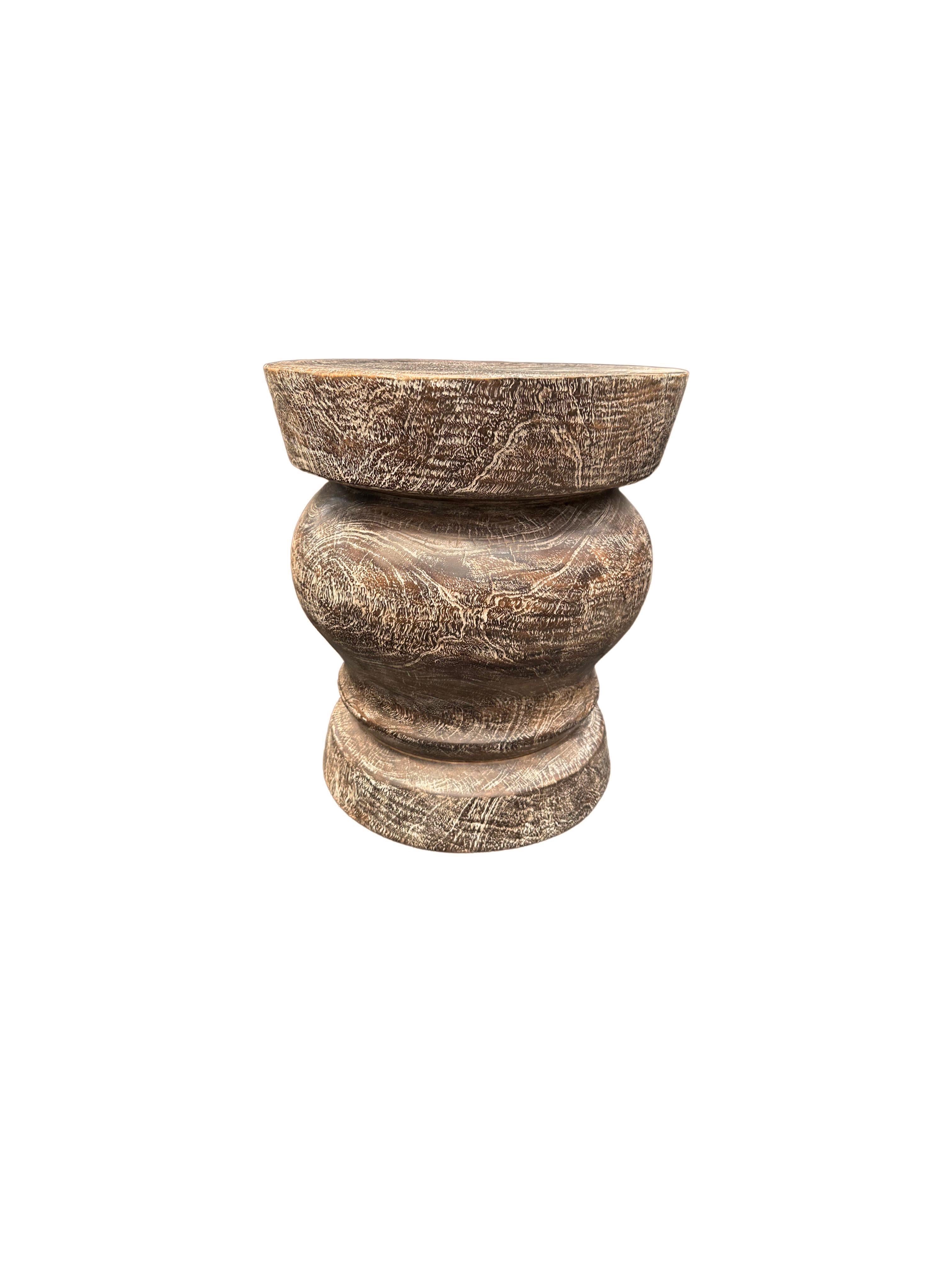 Une table d'appoint merveilleusement sculptée, fabriquée à partir d'un seul bloc de bois de manguier. Il présente de merveilleuses textures de bois. Cette table présente des détails sculptés qui enveloppent ses côtés. Pour obtenir sa finition brun
