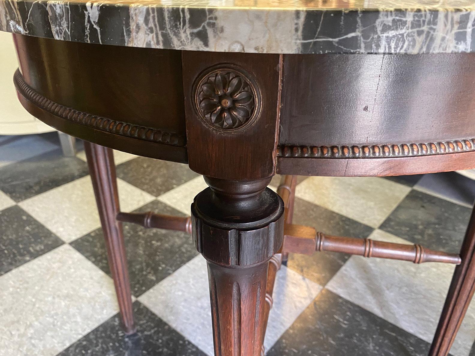 Vintage marble-top end-table. The marble is in shades of black, grey and white and is removable. It is original to the table. The base is solid wood with a fluted straight leg. See photos for the details in the carved wood base.