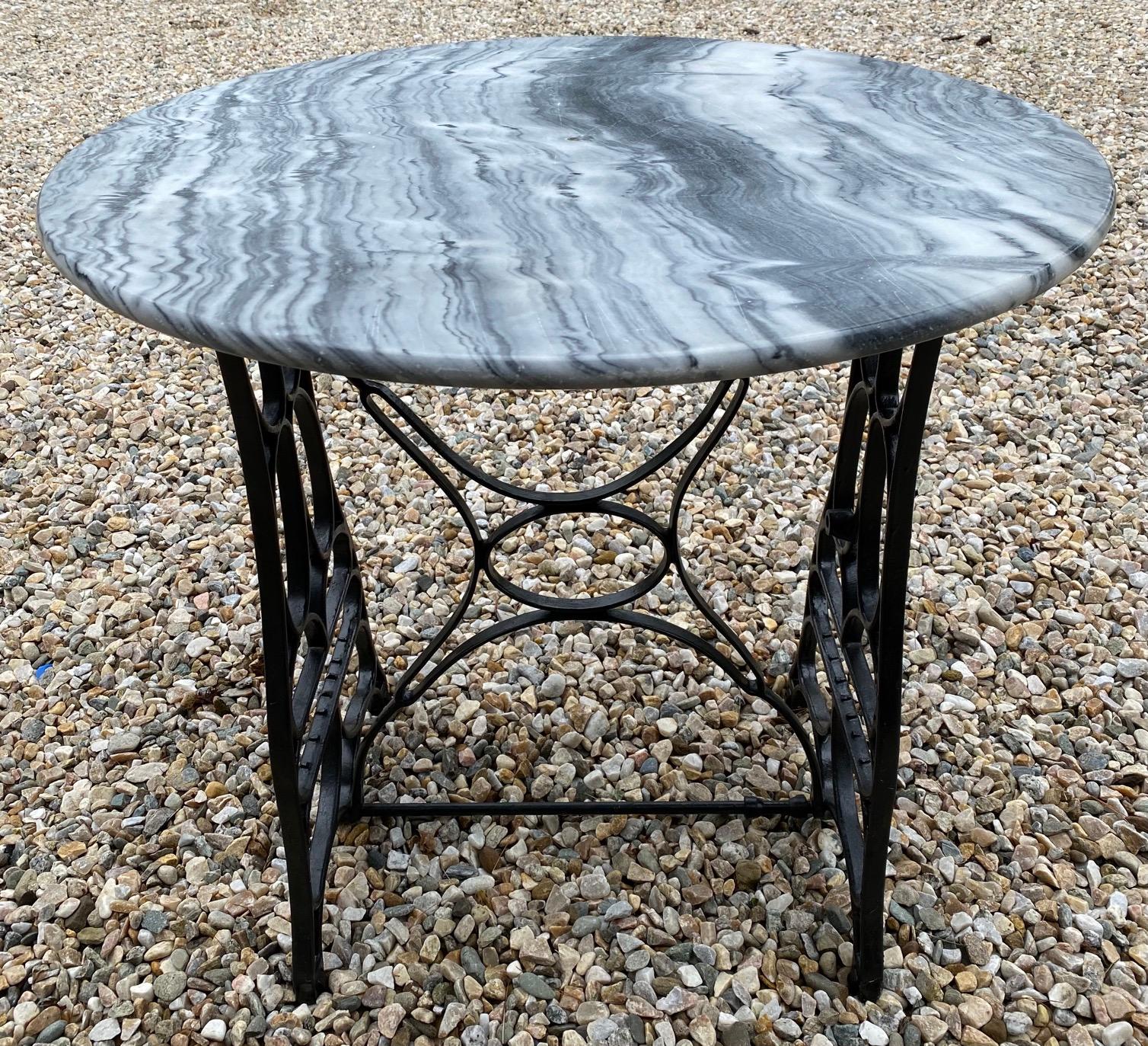 La table ronde unique à plateau en marbre est dotée d'une base de machine à coudre antique transformée en base de table. Le plateau en marbre présente de belles veines. Notez qu'il a une marque centrale à l'endroit où il est utilisé pour s'attacher