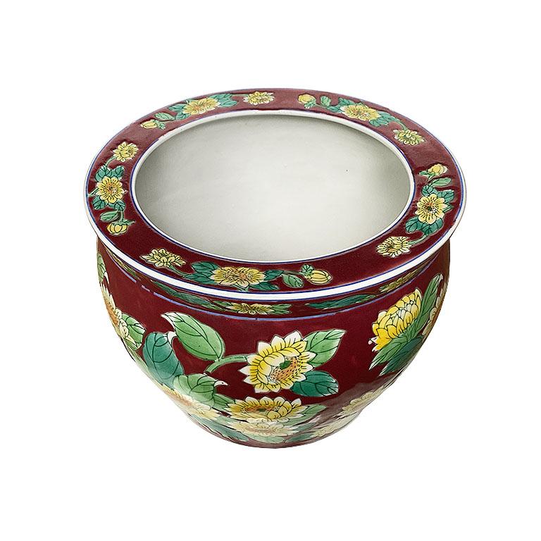 A pretty maroon chinoiserie Jardinière with a yellow floral motif. This planter will be a lovely accent to a patio or living room. It is glazed in a deep maroon background, with yellow flowers with lush green foliage. The rim at the top is decorated