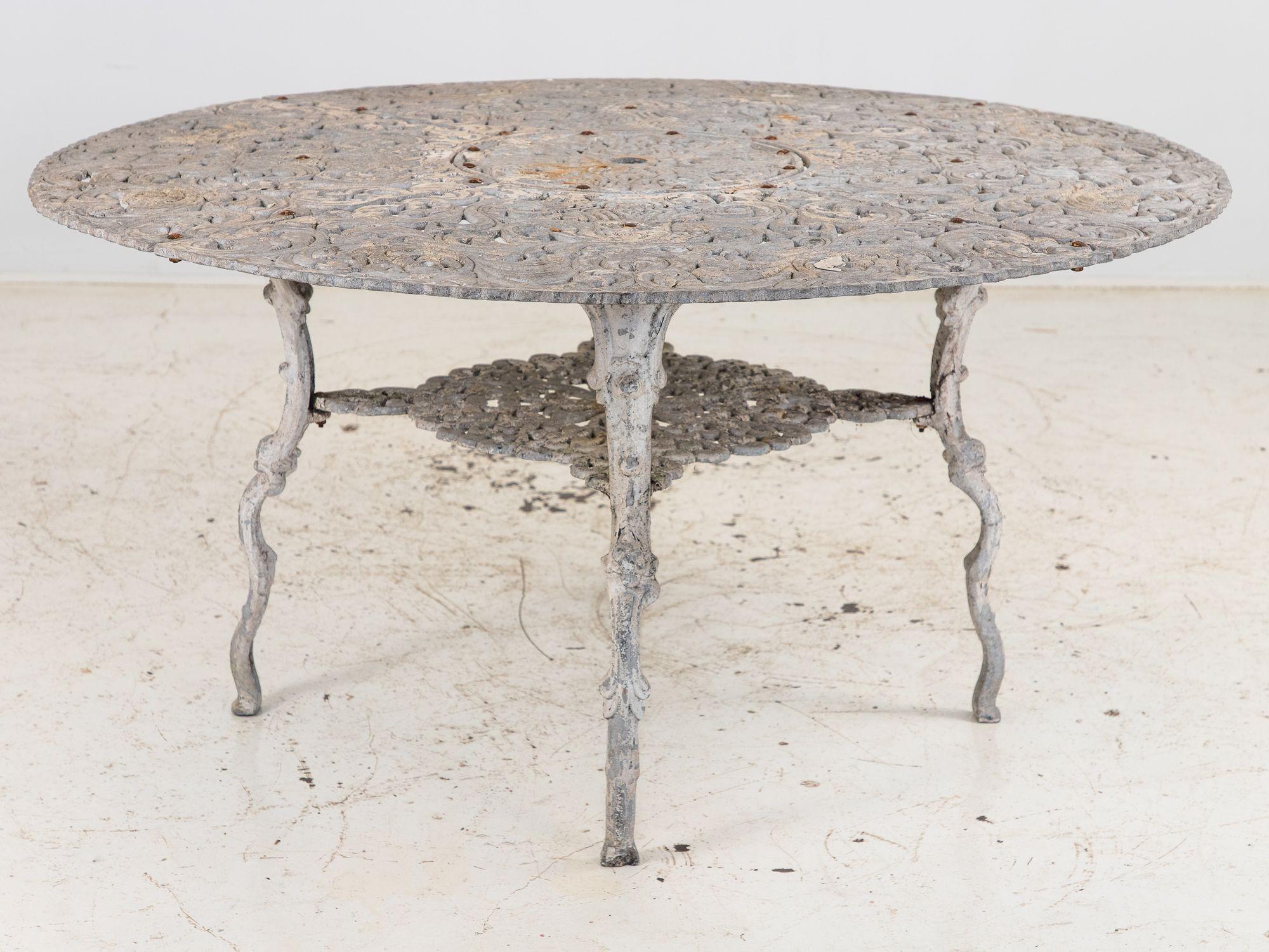 This 1960s Swedish cast aluminum garden dining table features a beautifully detailed round top adorned with a repeating acanthus leaf and scrollwork design, accented by a scalloped edge. A second tier connects the four legs, providing stability and