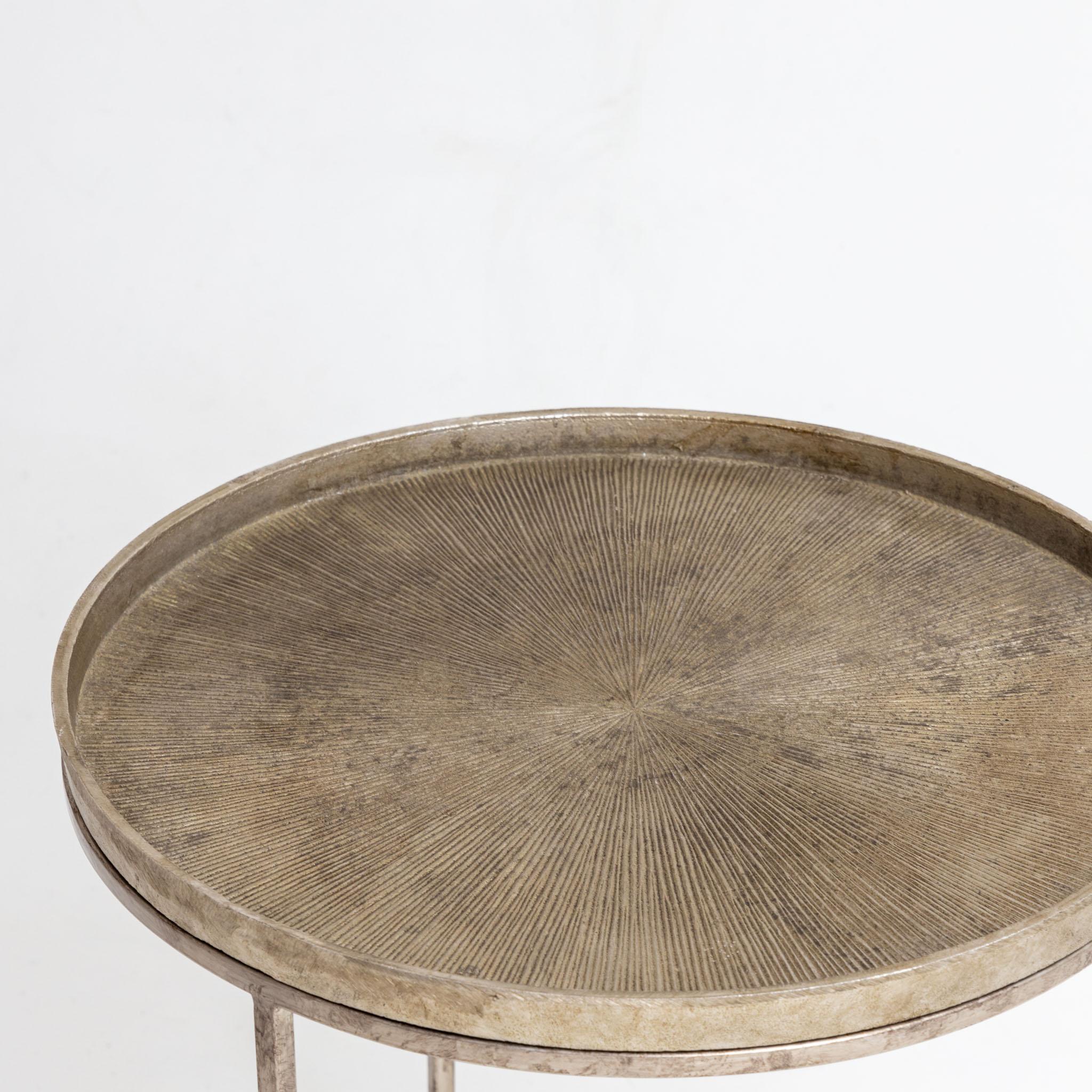 Round metal side table with radial textured table top with narrow rim and three-legged base.