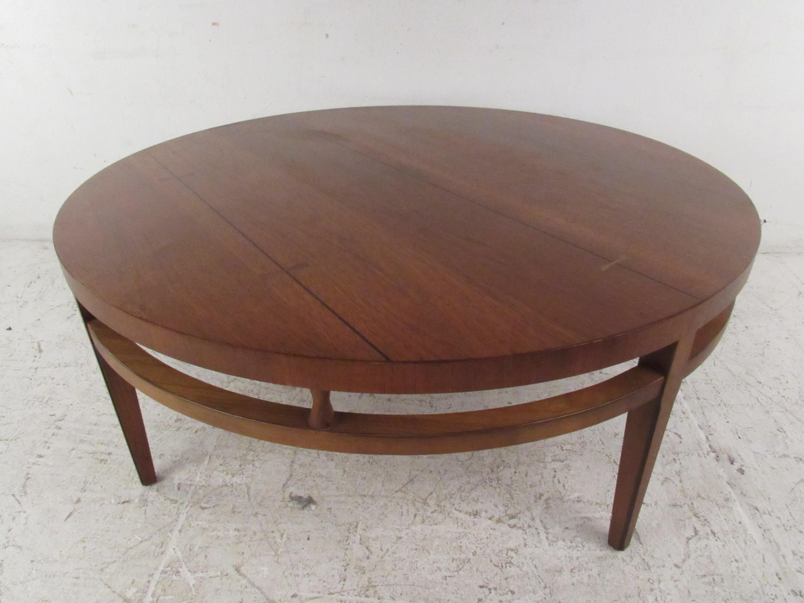 This stunning vintage modern coffee table boasts a circular shape with a stretcher wrapping all the way around. A sleek design with sculpted hourglass fixtures placed between the top and the stretcher. This handsome piece with a vintage walnut