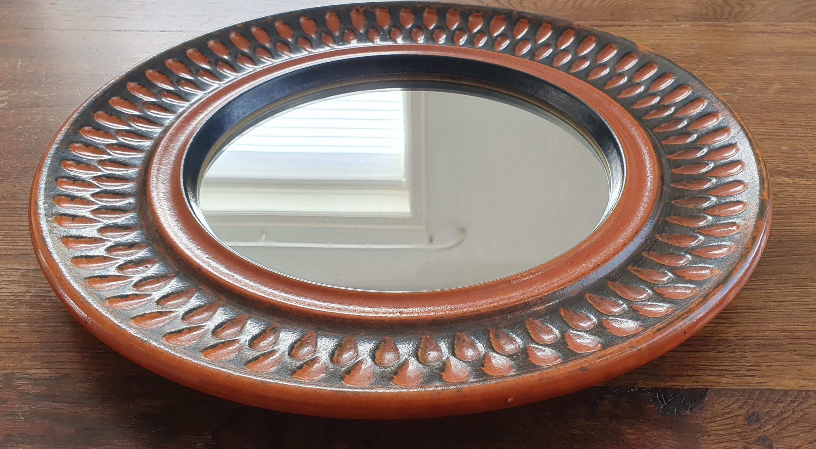 Etched round ceramic wall mirror in orange and brown glaze. In good vintage condition.