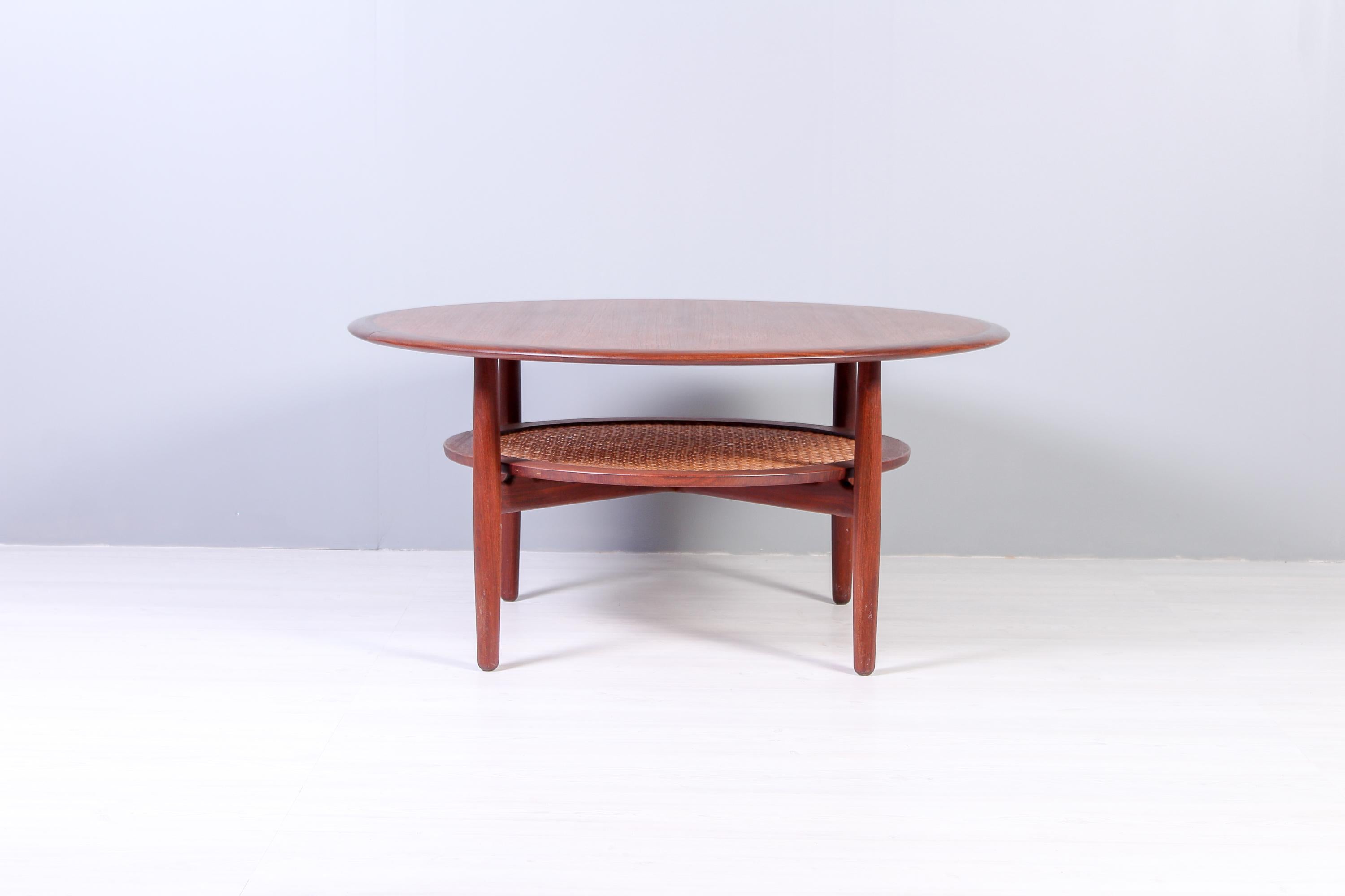 A round Danish coffee table produced in the 1950s. The table is made out of teak with a cane shelf. Very decorative and high quality. 

Very good vintage condition with refinished top and only few small breakage on cane.