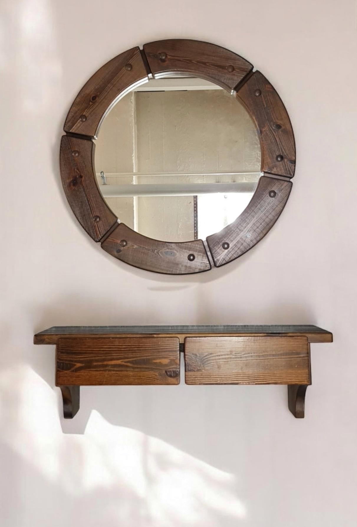 A beautiful console set in dark pine made of a round mirror and a two drawer hanging shelf. The set has a slightly brutal feel to it, but is quite calm and would fit perfectly in modern and eclectic interiors, in addition to rustic or cottage